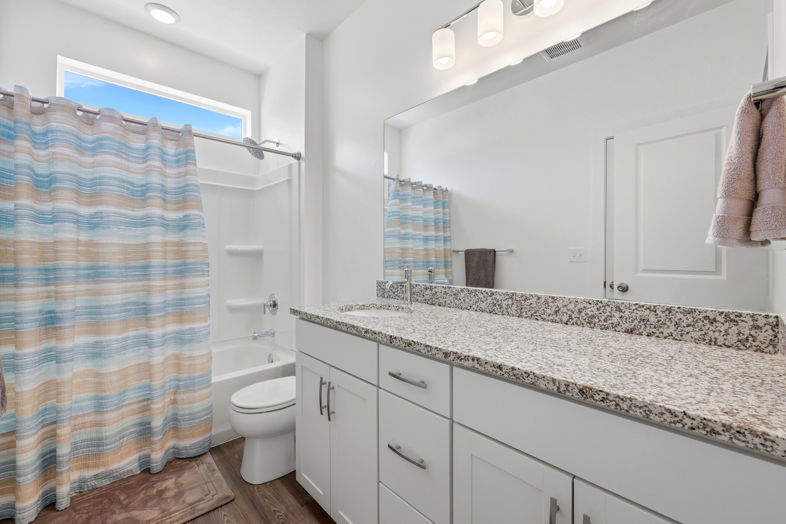 Bathroom featuring a white vanity with granite-style countertop, dual sinks, and white cabinetry with brushed nickel hardware