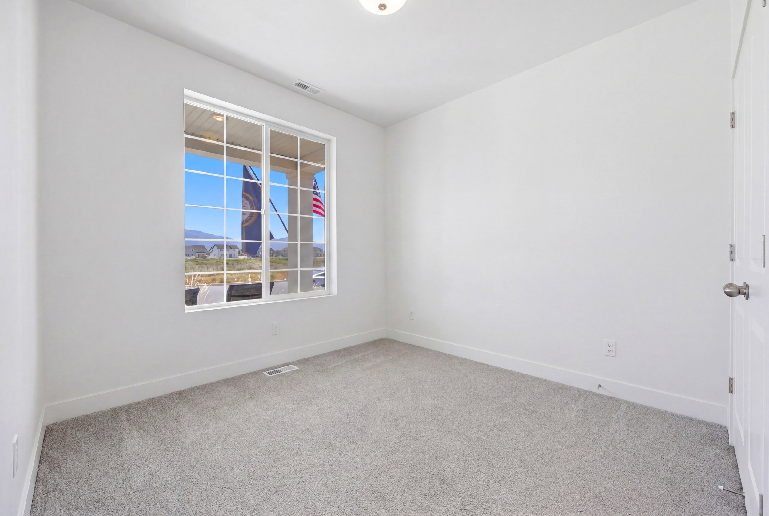Room featuring light gray carpeting, crisp white walls, a multi-pane window, and a flush-mount ceiling light