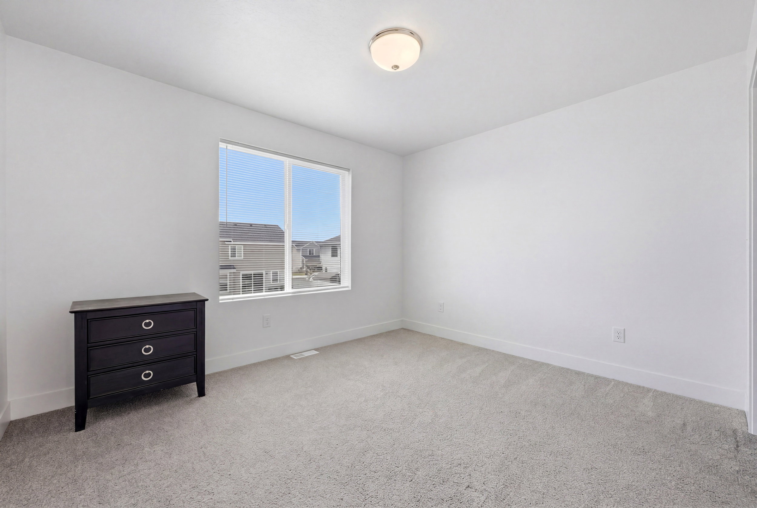 Windowed interior space featuring light-colored walls, grey carpeting, and white baseboards