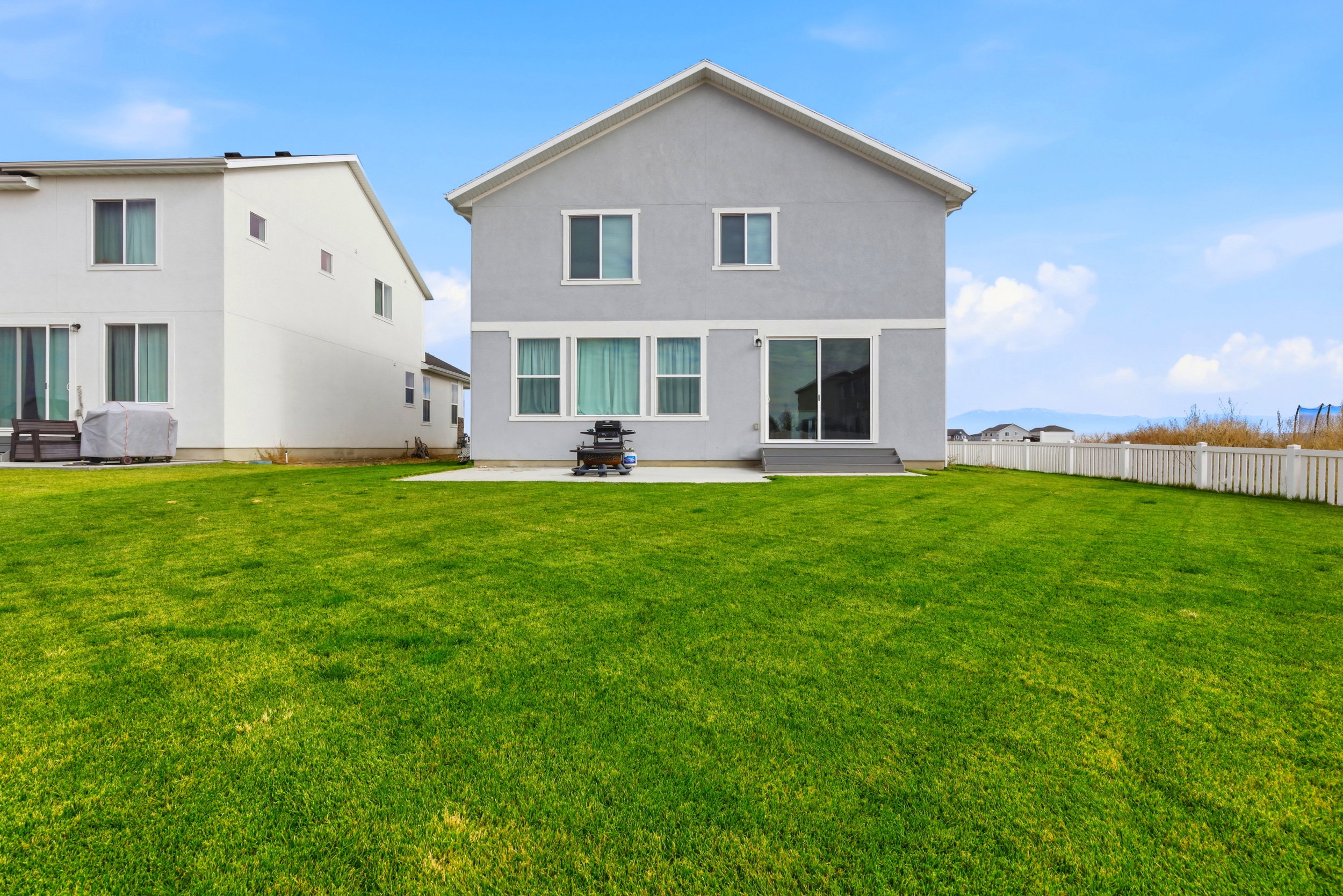 Spacious backyard featuring a large green lawn, concrete patio, and a white picket fence