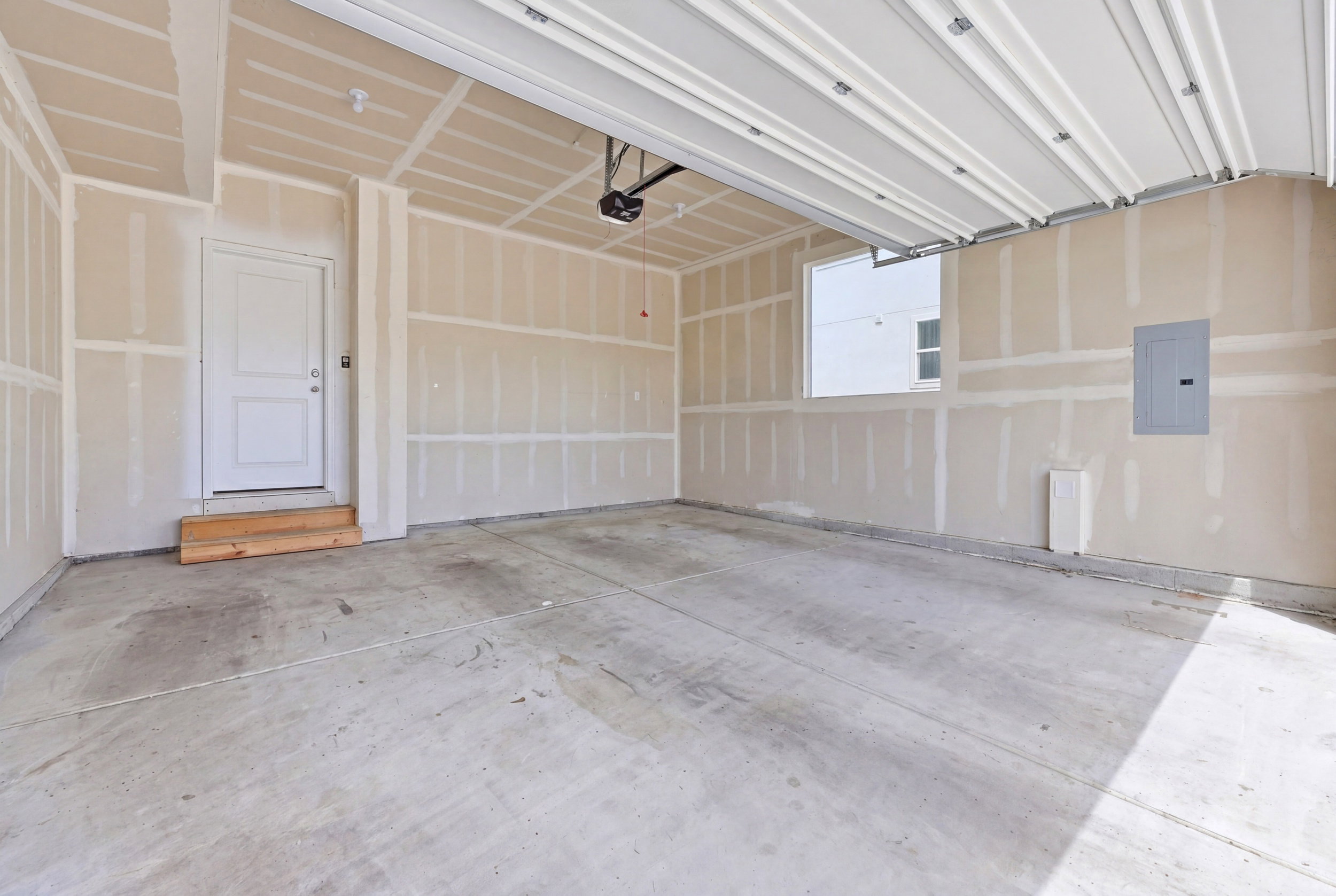 Spacious garage featuring a concrete floor, an overhead door, and an interior access door with wooden steps