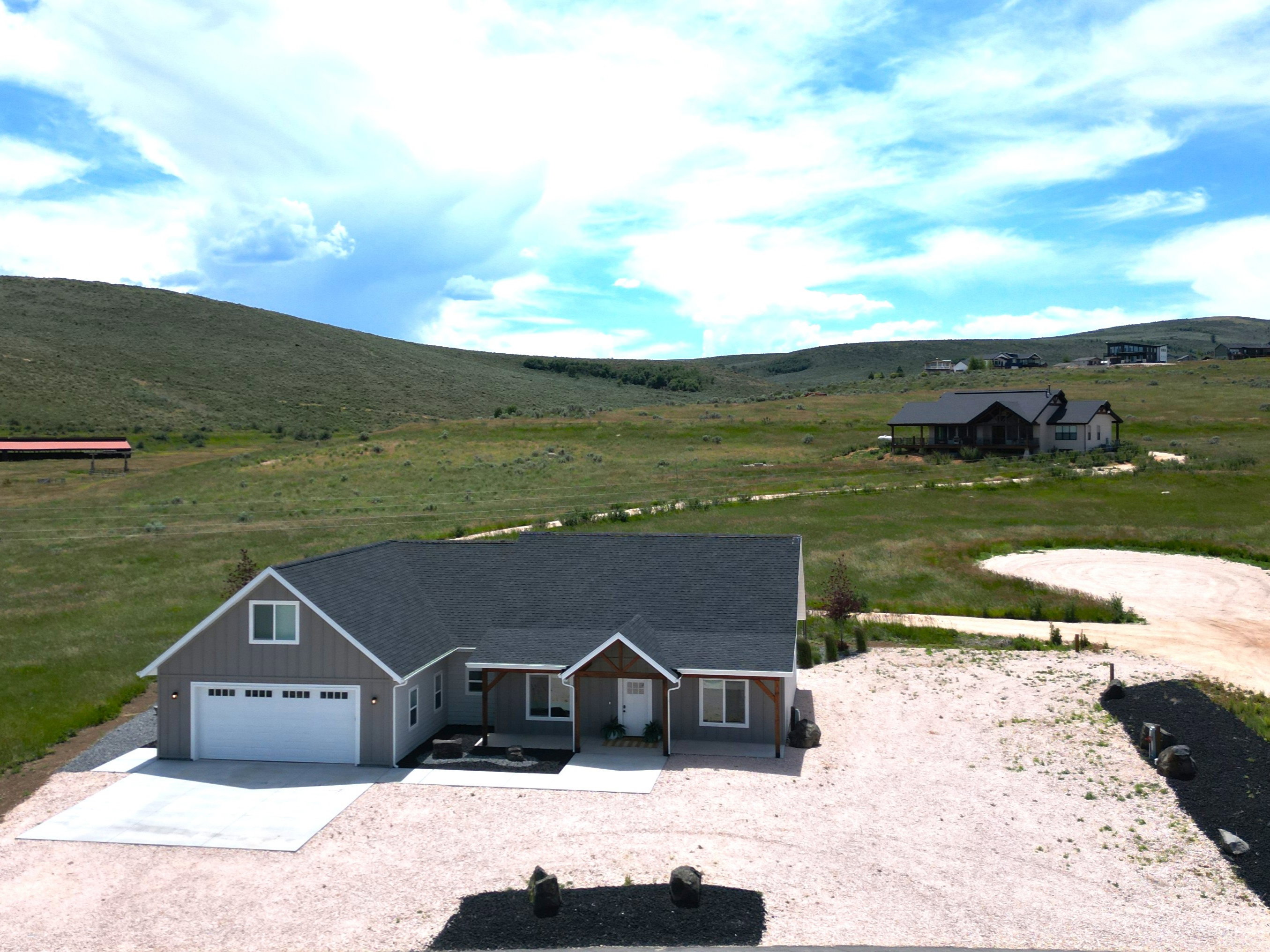 Contemporary ranch-style residence featuring horizontal grey siding, a dark shingle roof, a two-car garage with a white door, a covered front porch with wood-wrapped columns, and a concrete driveway