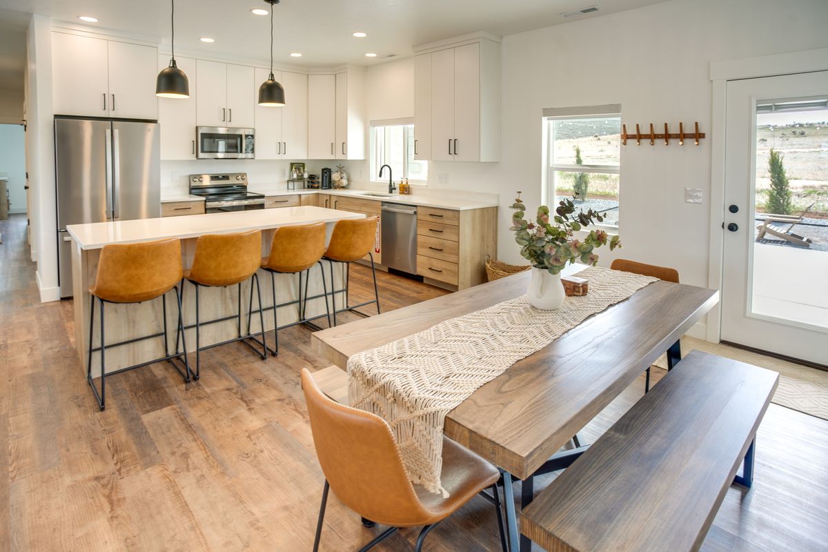 Open-concept kitchen and dining area featuring a spacious island with pendant lighting, stainless steel appliances, wood-finish flooring, white cabinetry, and a glass-paned exterior door