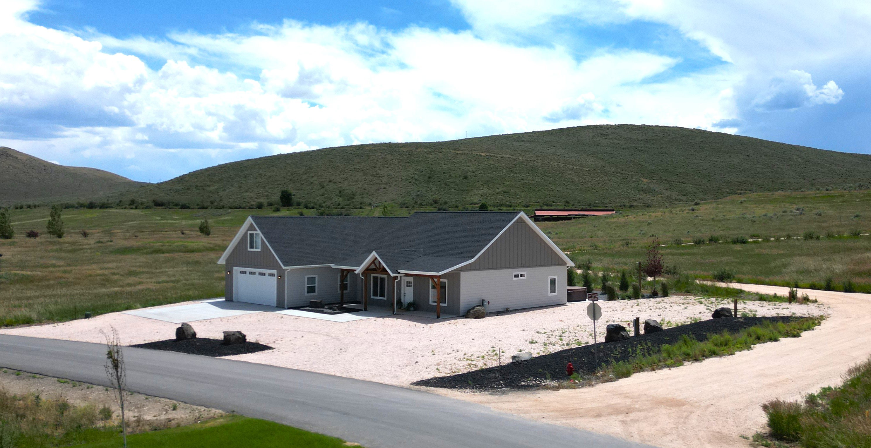 Contemporary single-story home featuring a two-car garage, dark gray shingle roof, and light gray siding with vertical accent panels