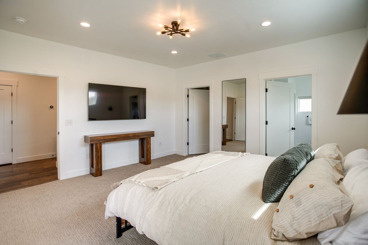 Spacious bedroom featuring light-colored carpeting, white walls, and a modern ceiling light fixture