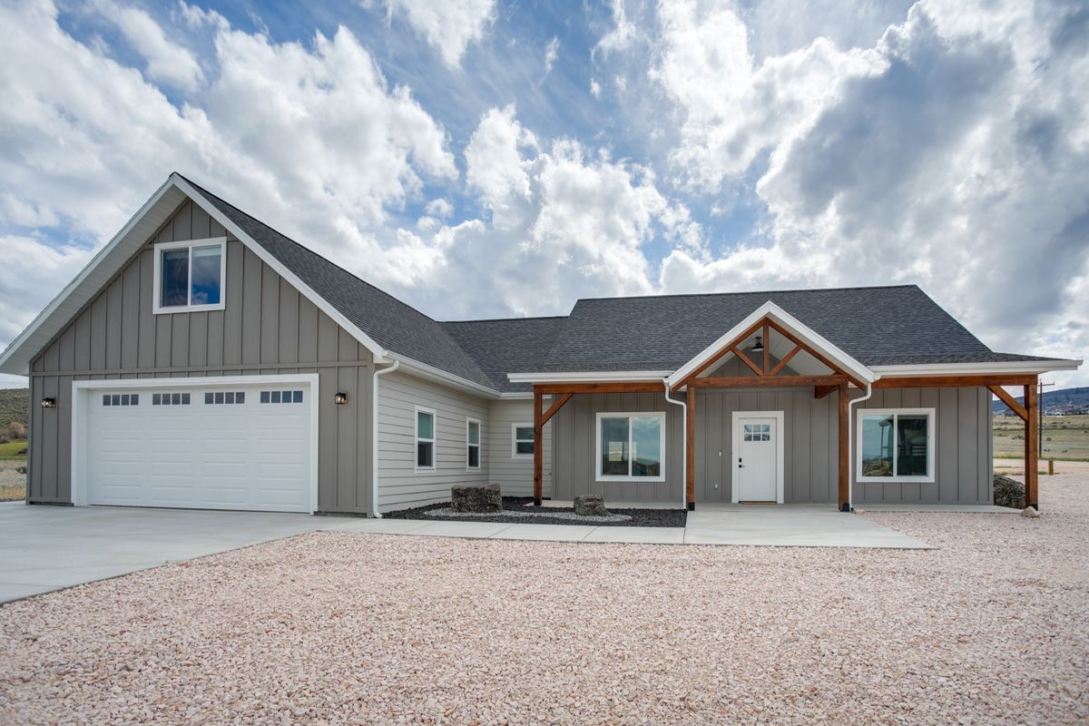 Contemporary exterior featuring light gray siding, dark asphalt shingles, a decorative timber frame porch, and an attached two-car garage with a white door