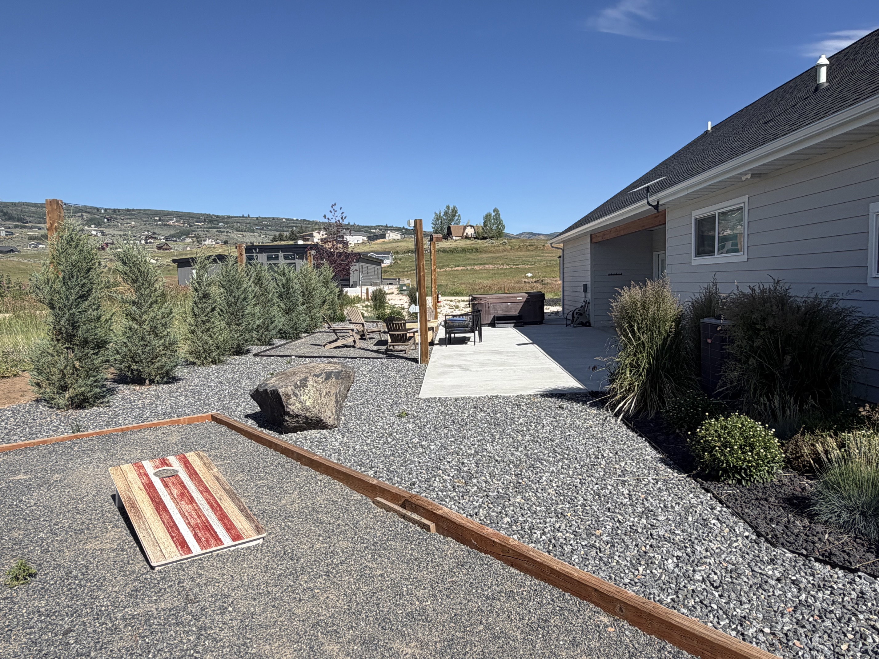 Spacious outdoor area featuring a concrete patio, pea gravel landscaping, mature evergreen plantings, and a covered back porch