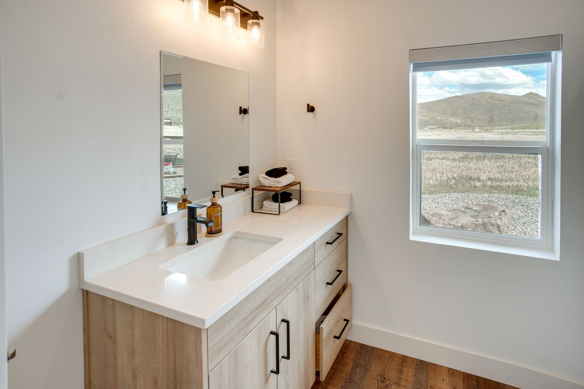 Modern bathroom vanity featuring light wood-finish cabinetry, a white countertop, and an undermount sink with a matte black faucet