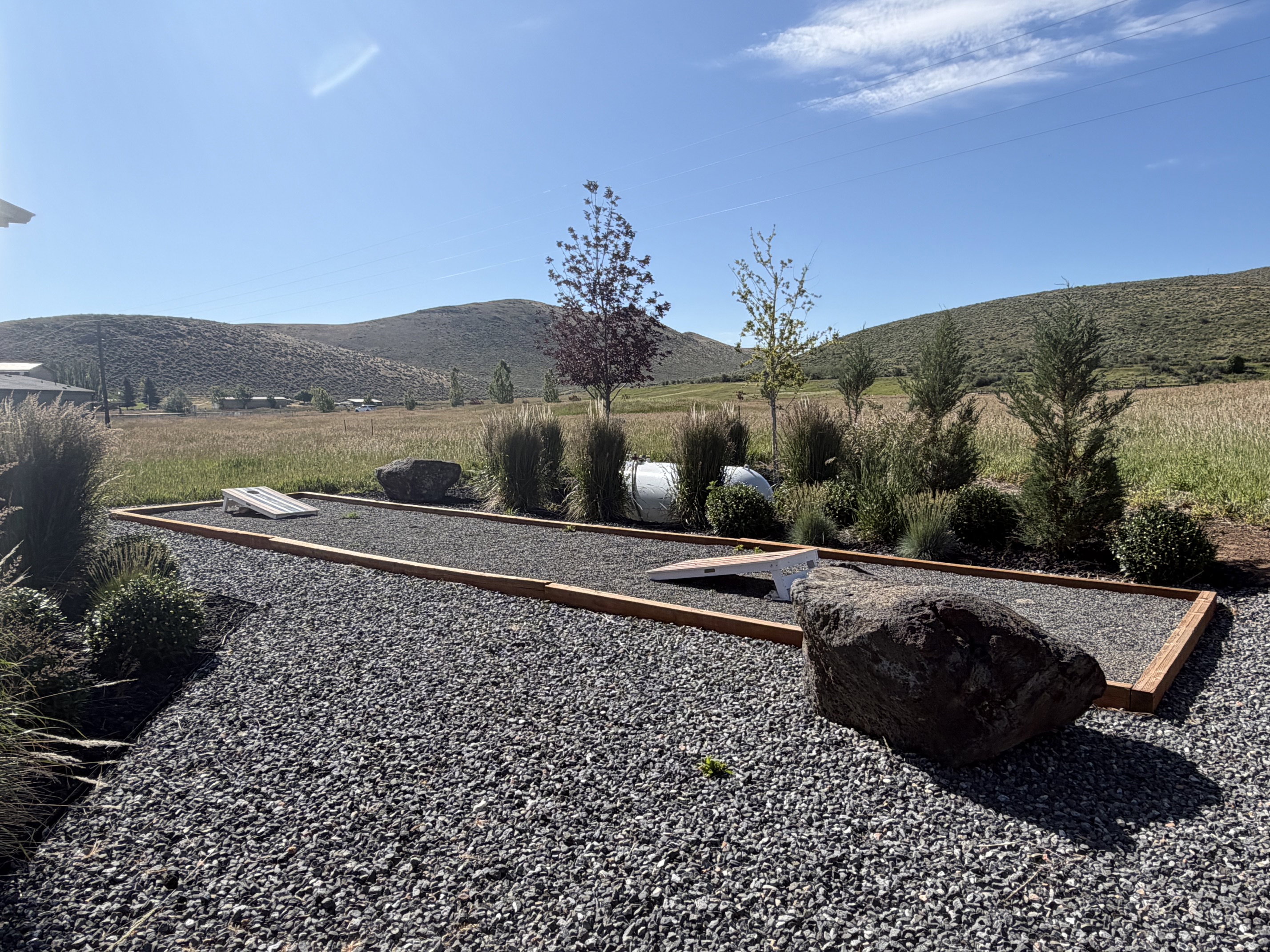 Gravel-covered outdoor recreation area featuring a built-in cornhole court with timber framing