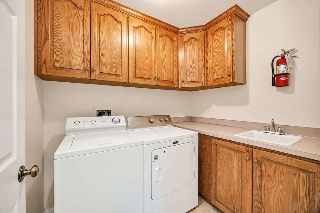 Main level laundry area featuring wood cabinetry, laminate countertops, an integrated sink with a chrome faucet, and ample overhead storage