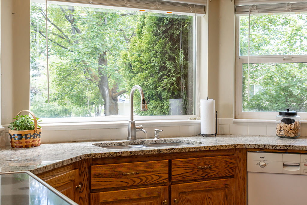 Kitchen featuring a double basin sink with a high-arch faucet, granite countertops, wood cabinetry, and a built-in dishwasher