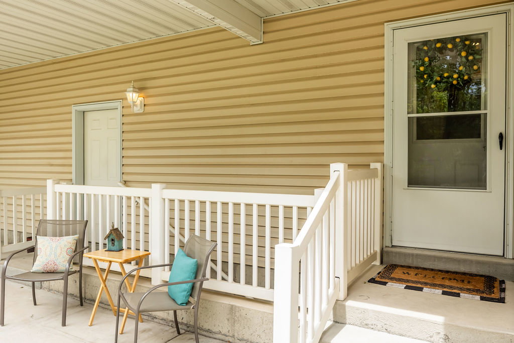 Covered south facing patio featuring beige horizontal siding, white railing, and exterior lighting