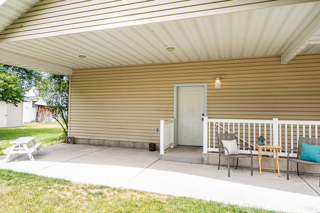 Covered patio with concrete flooring, beige vinyl siding, entry door to the garage, an exterior wall light fixture, and exterior stairs leading to the basement