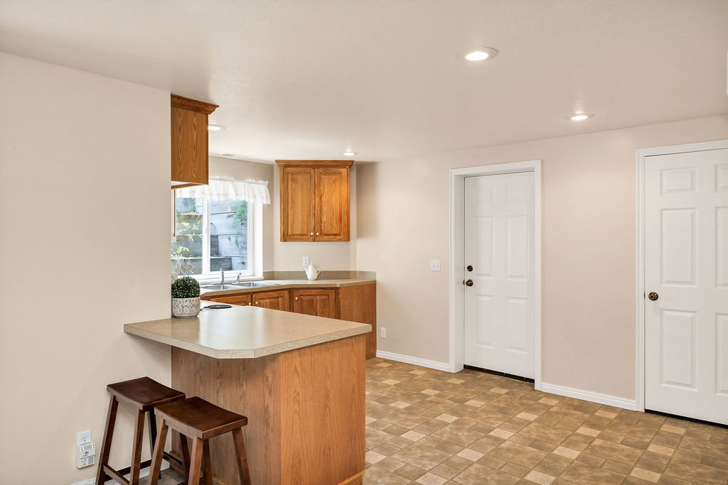 Basement kitchen featuring recessed lighting, a breakfast bar with a light-toned countertop, wood-finish cabinetry, and laminate flooring