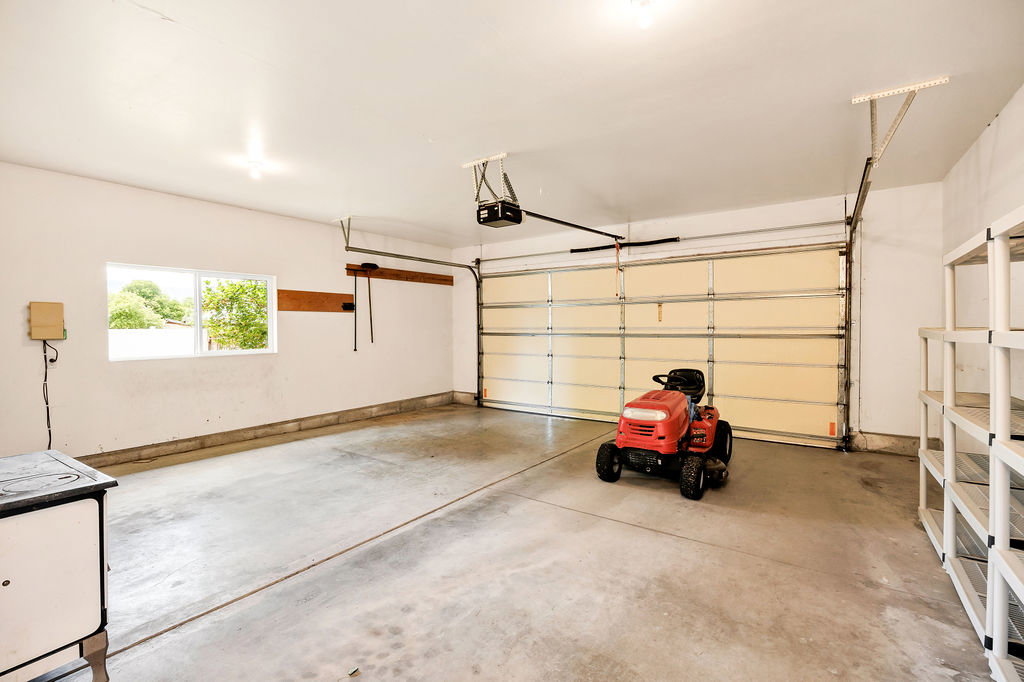 Spacious garage featuring a concrete floor, overhead lighting, and a single window, storage shelves included