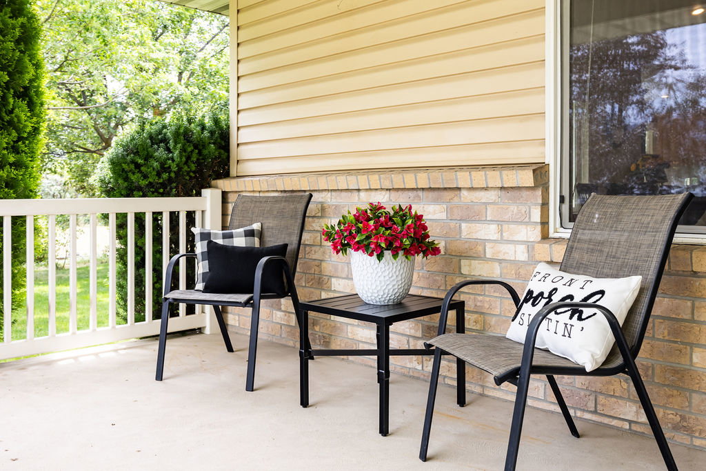Inviting extra large front porch featuring a white railing, concrete flooring, and a brick facade with horizontal siding