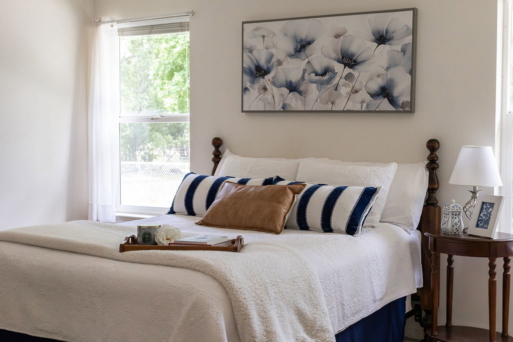 Bright primary bedroom featuring large windows with sheer curtains, a dark wood-finish bed frame, and light-toned walls