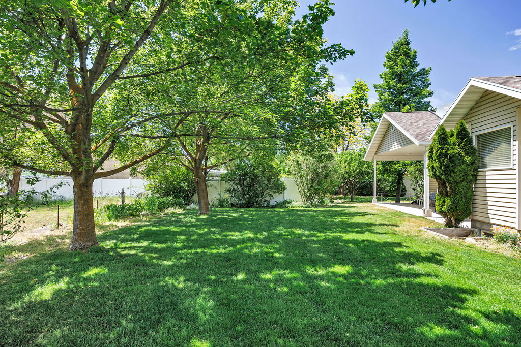 Expansive south lawn featuring mature shade trees, a covered patio, vinyl siding, and established landscaping