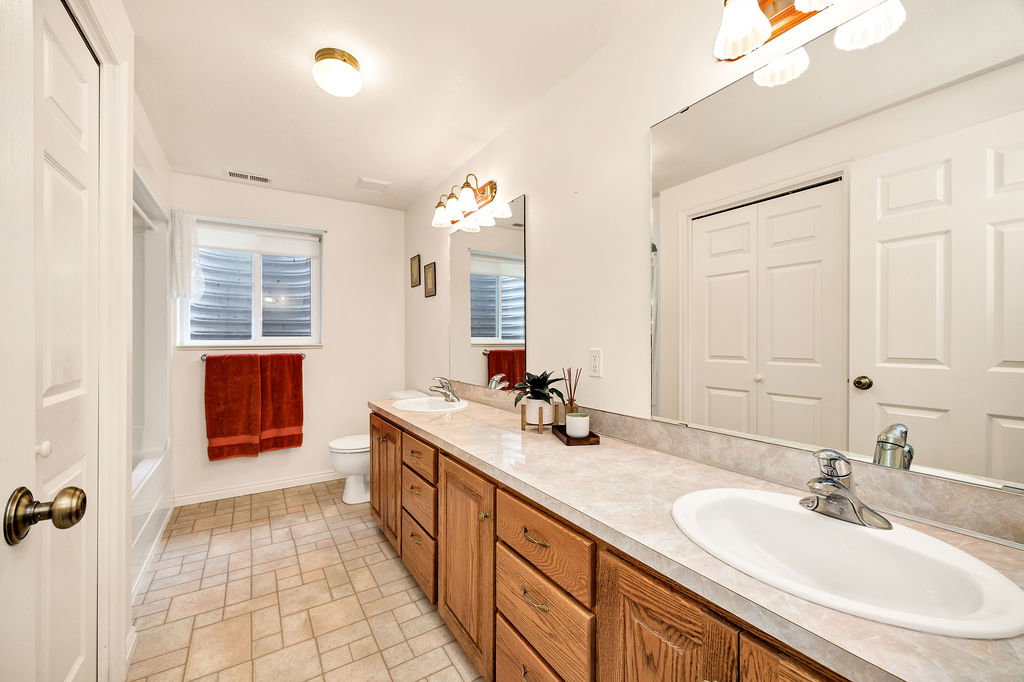 Basement bathroom featuring a long wood-finish vanity with two integrated sinks, an expansive countertop, and a large mirror