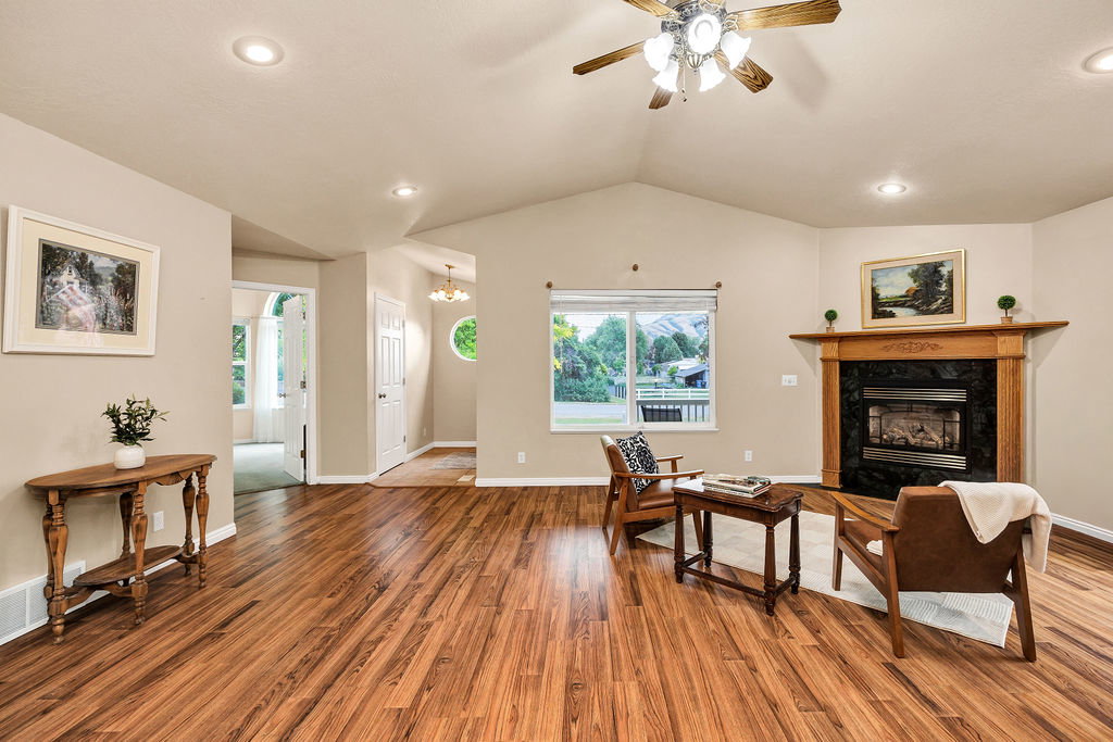 Spacious living area featuring vaulted ceilings, wood-finish flooring, a fireplace with a wood mantel and dark stone surround, and recessed lighting
