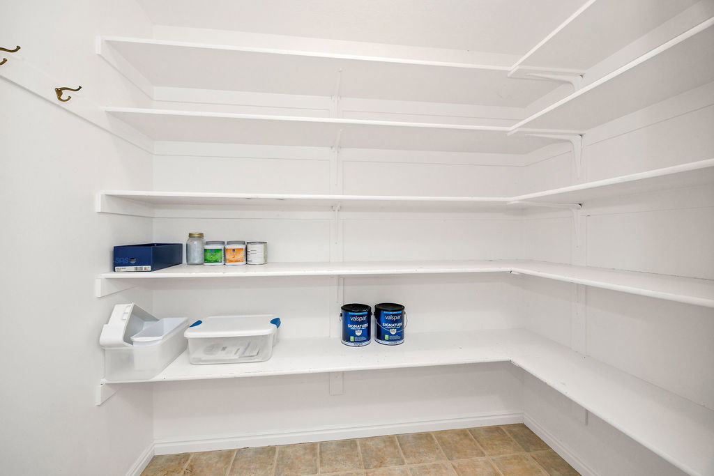 Expansive walk-in pantry featuring white shelving, a full-height wall of shelving, and tile flooring