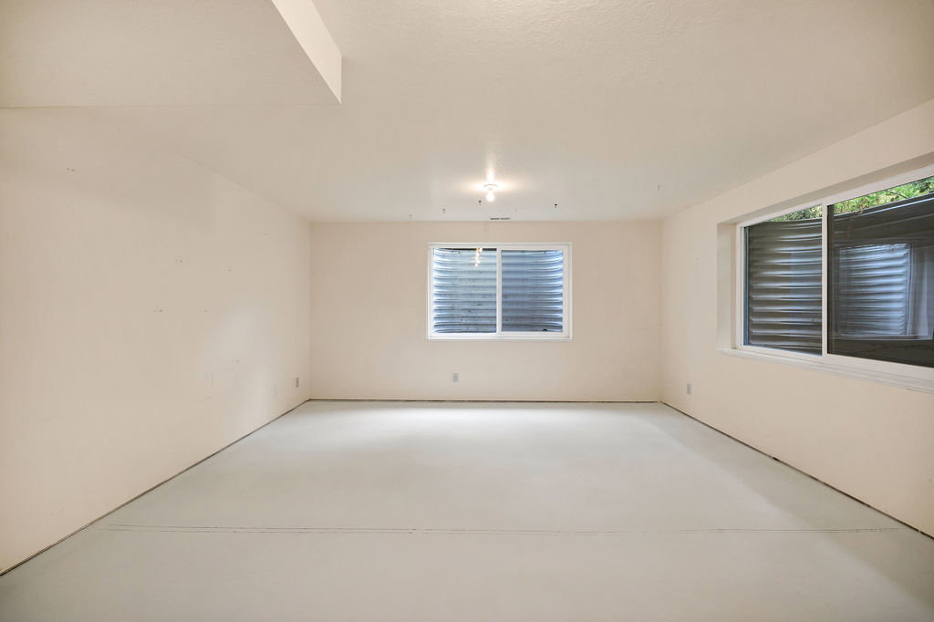 Spacious 3rd bedroom featuring light-toned walls, a painted concrete floor, and multiple windows, just needs flooring