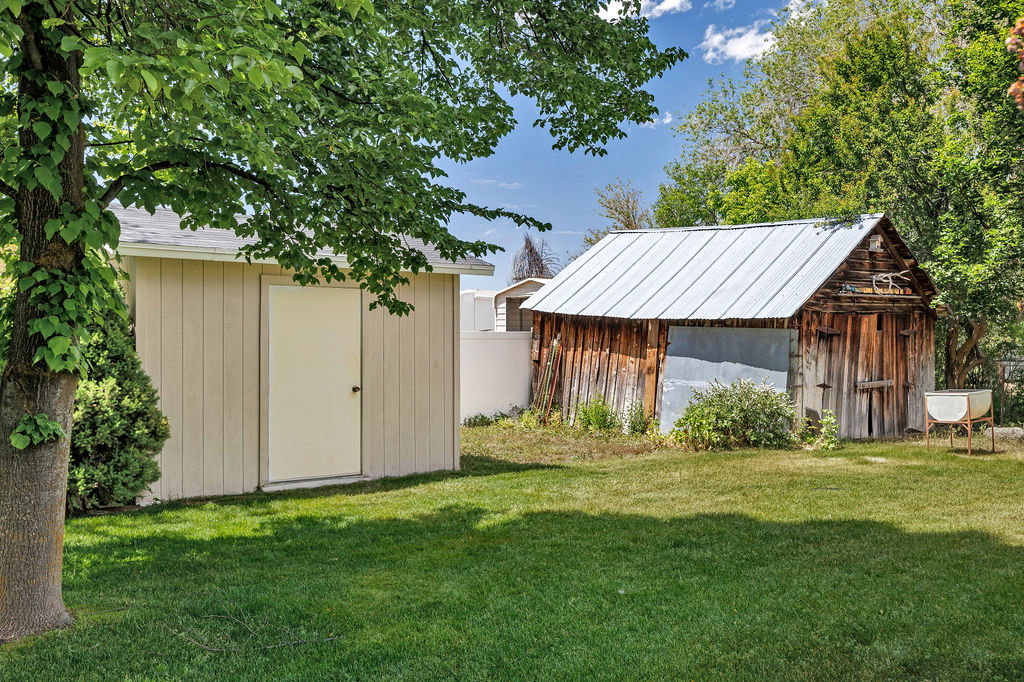 Expansive grassy backyard featuring a light-colored storage shed with a white door and a rustic wood barn with a metal roof