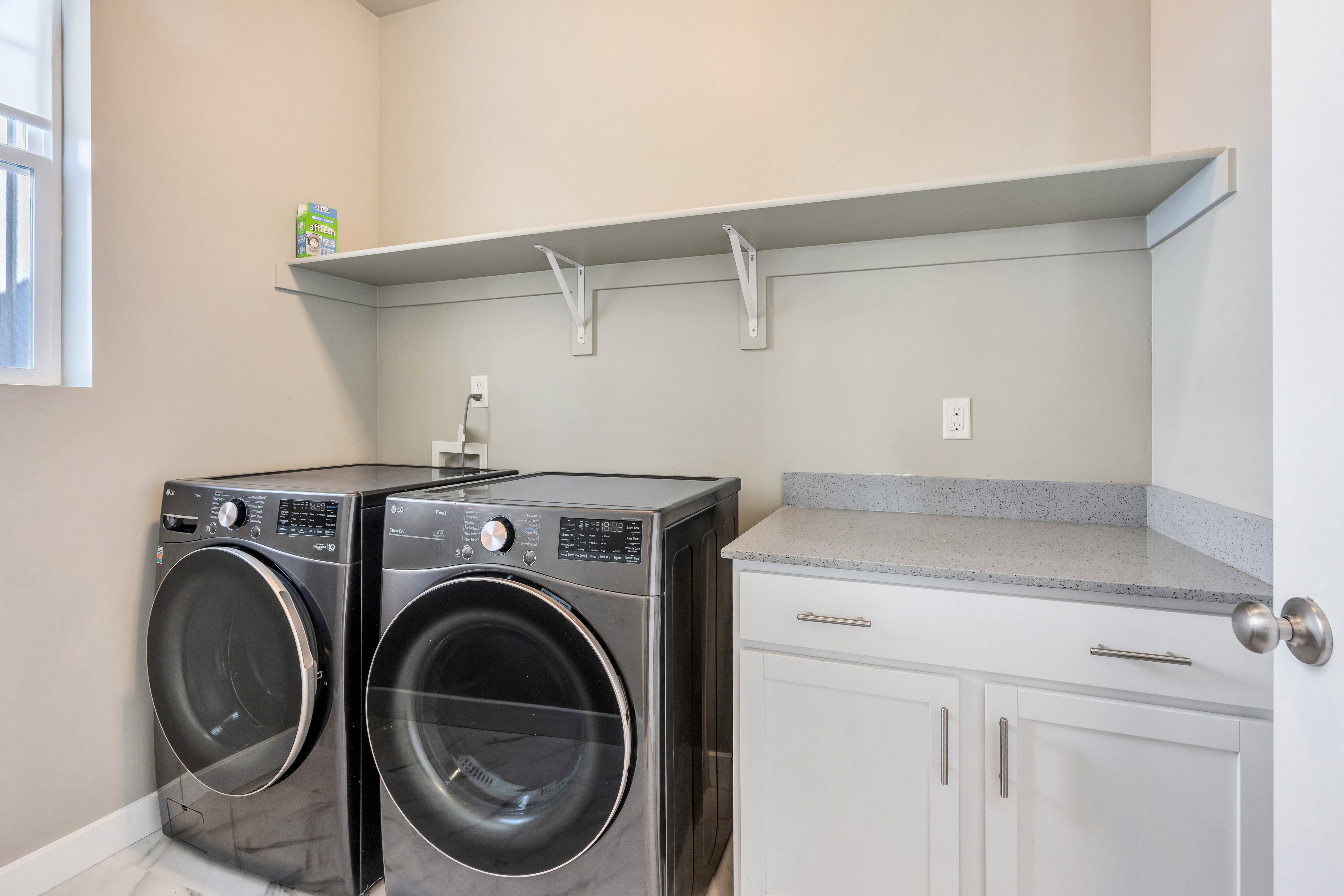 Dedicated laundry area featuring white shaker-style cabinetry, a speckled countertop, and an overhead shelving unit