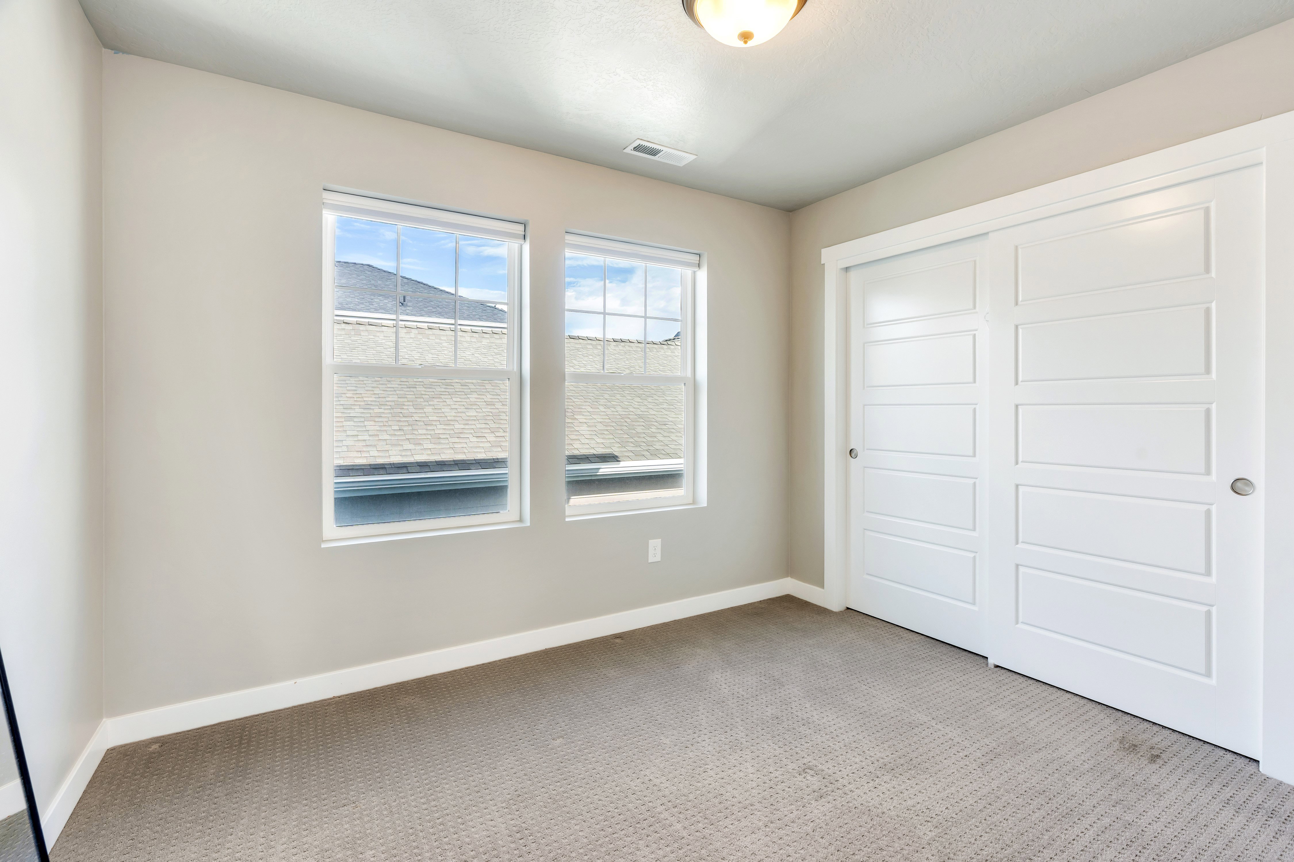 Interior room featuring two large windows, neutral wall tones, white baseboards, and a textured carpet