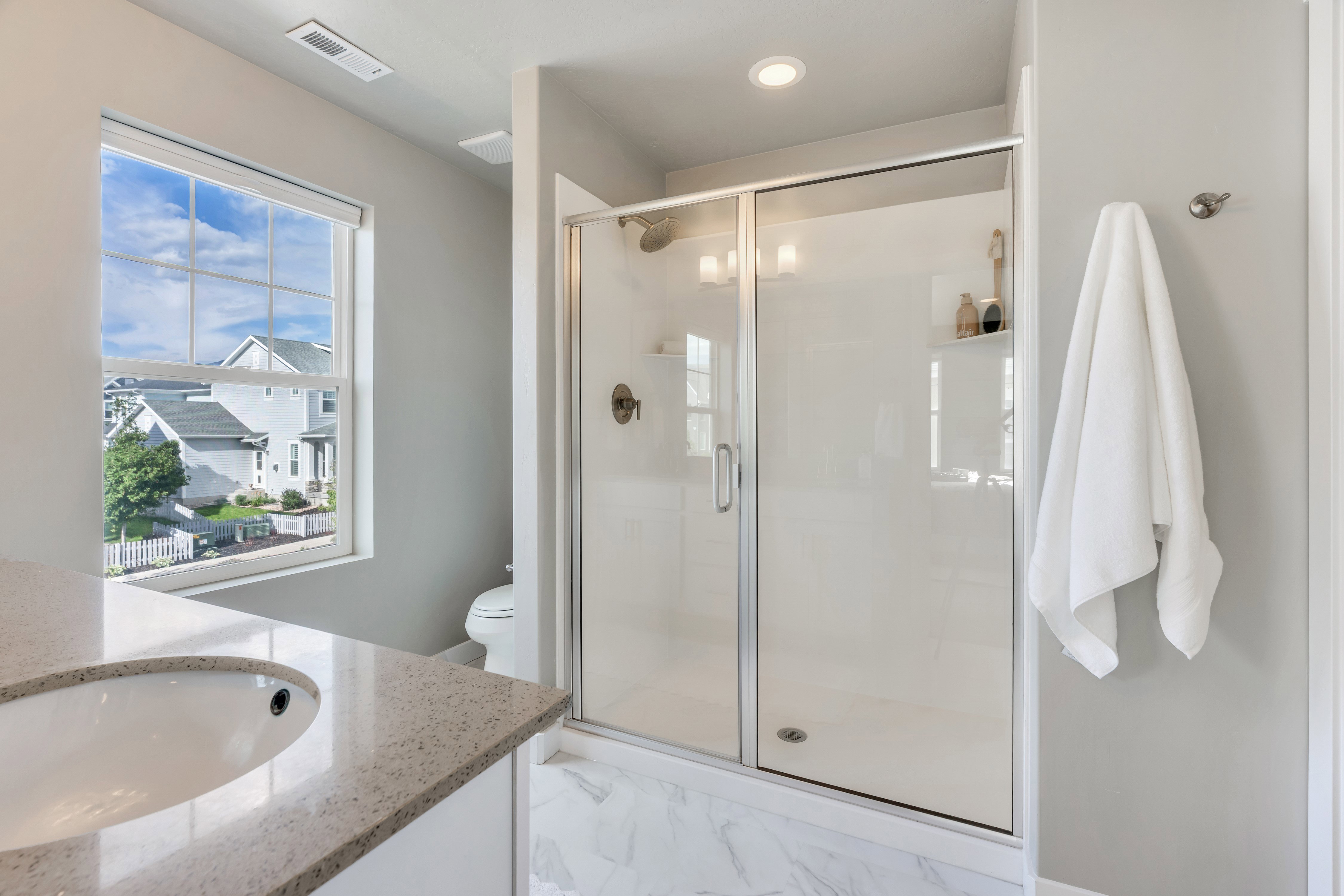 Bathroom featuring a glass-enclosed shower with a chrome fixture, a single vanity with an integrated sink and light-colored countertop, and a window with white trim