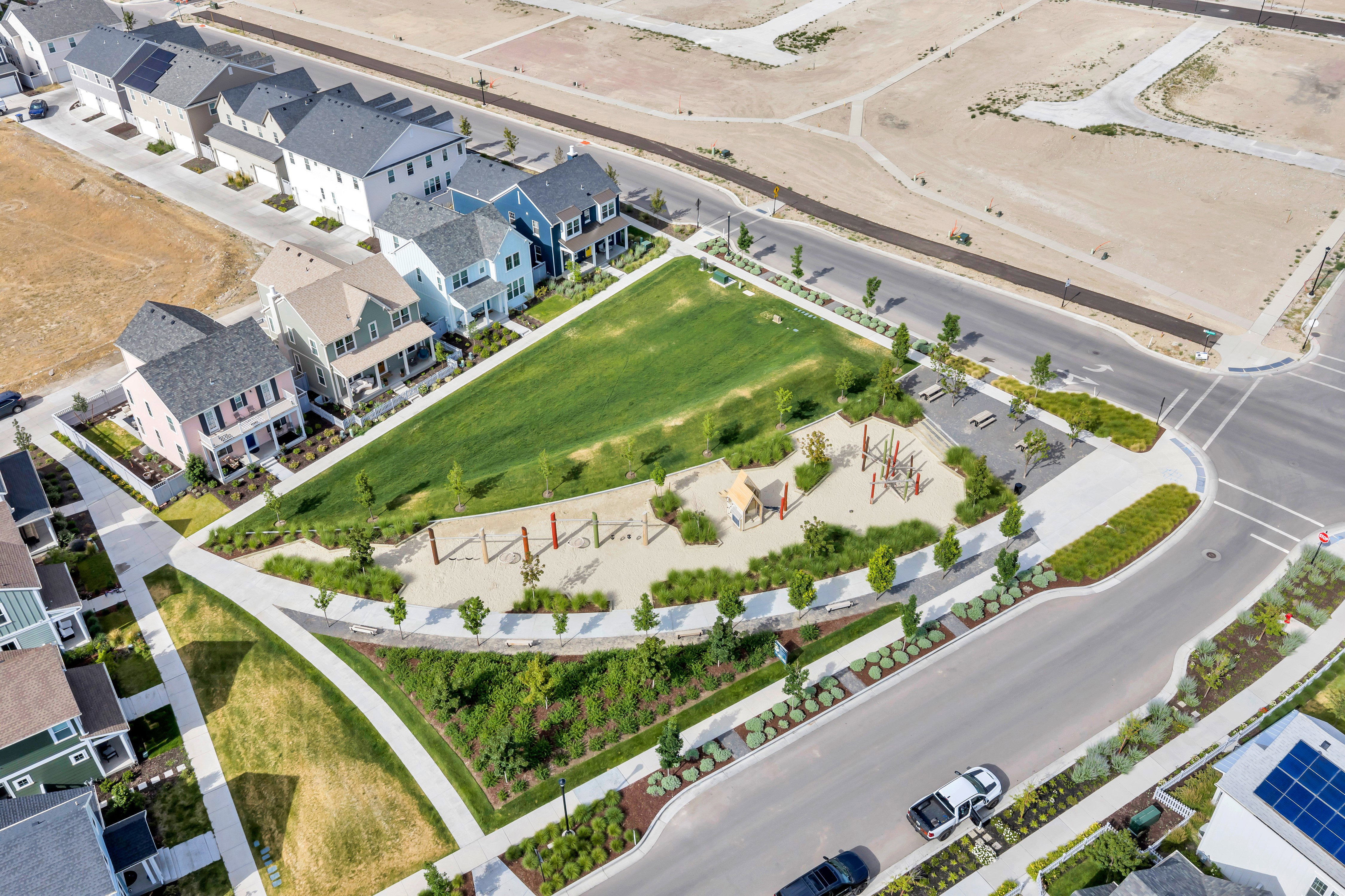 Community green space featuring a manicured lawn, playground area with sand base, paved walking paths, established landscaping, and street parking