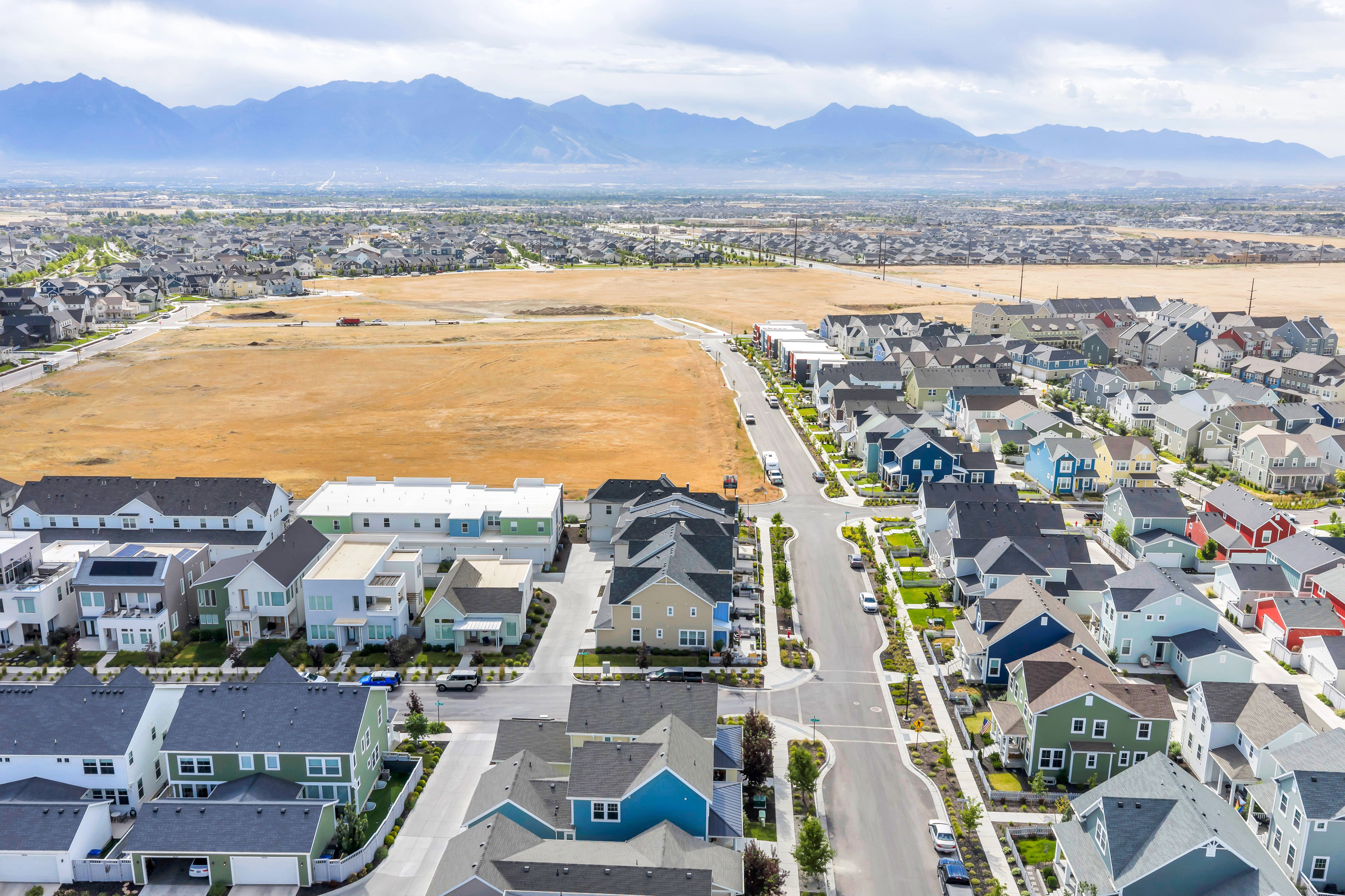 Newly developed neighborhood featuring diverse architectural styles, paved streets, and manicured landscaping, all framed by distant mountains