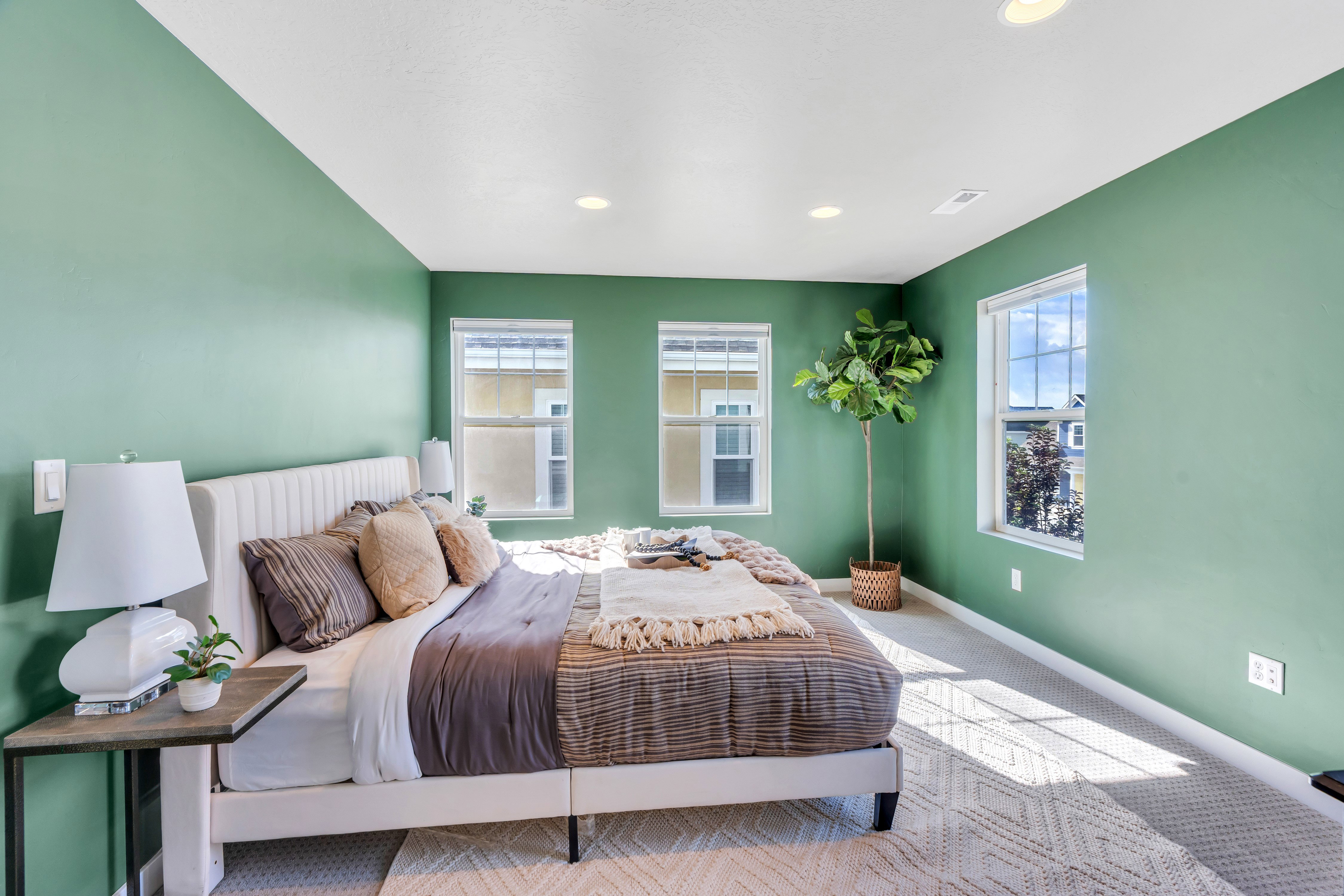 Bedroom featuring light green walls, three windows, white trim, and recessed lighting
