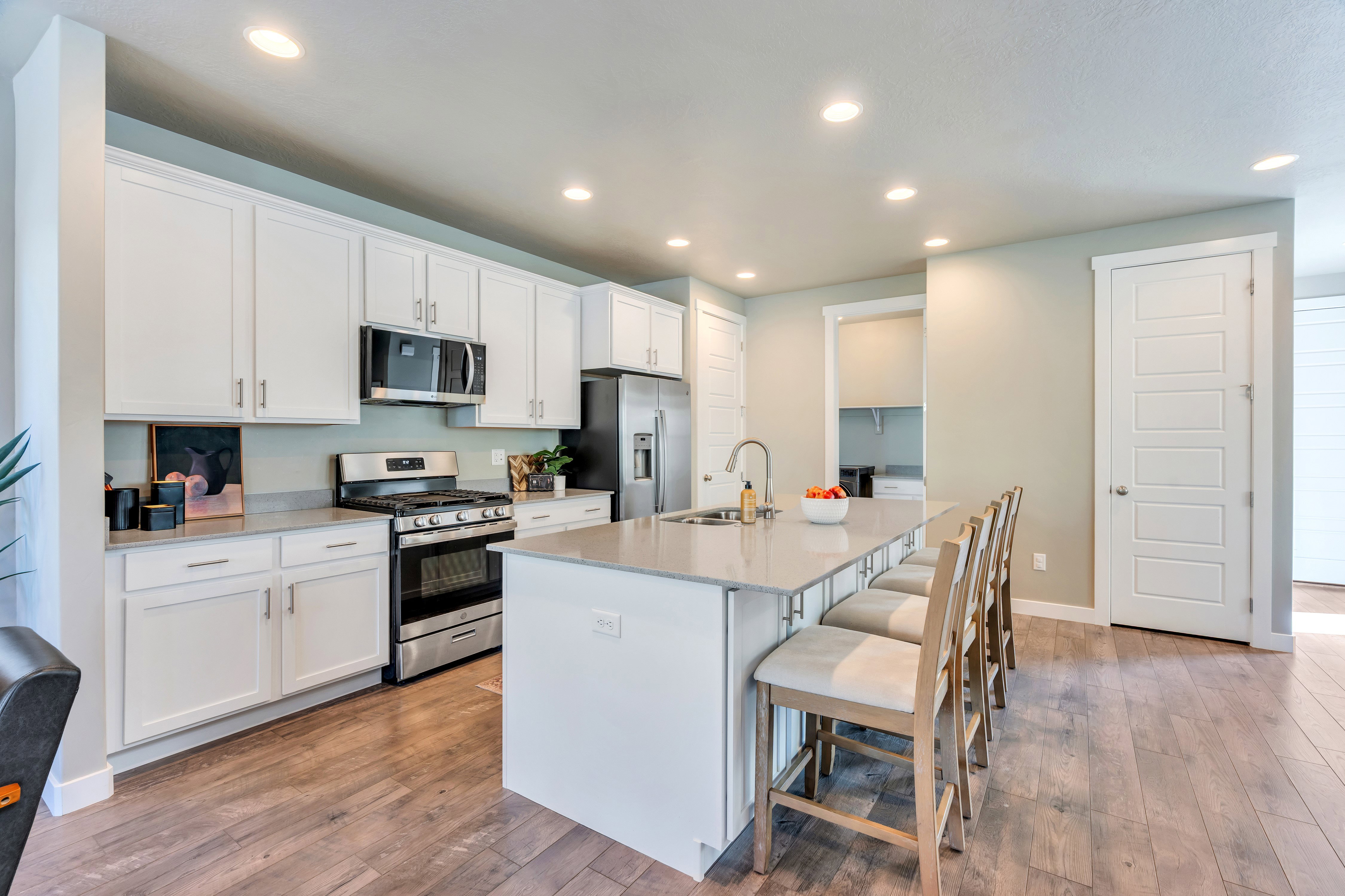 Modern kitchen featuring an expansive center island with seating, white shaker cabinetry, stainless steel appliances, and wood-finish flooring