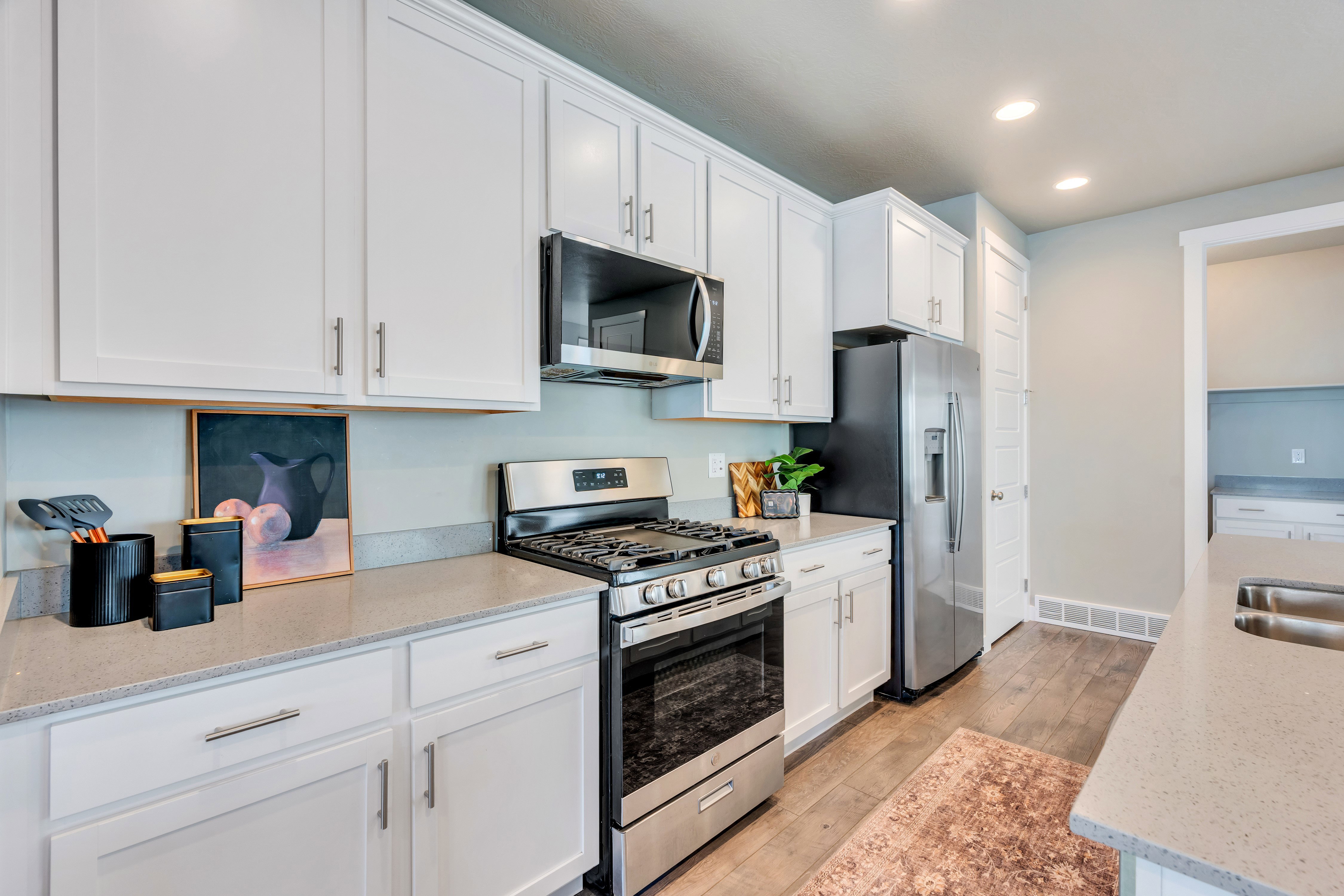 Modern kitchen featuring white cabinetry, stainless steel appliances, stone countertops, and wood-finish flooring