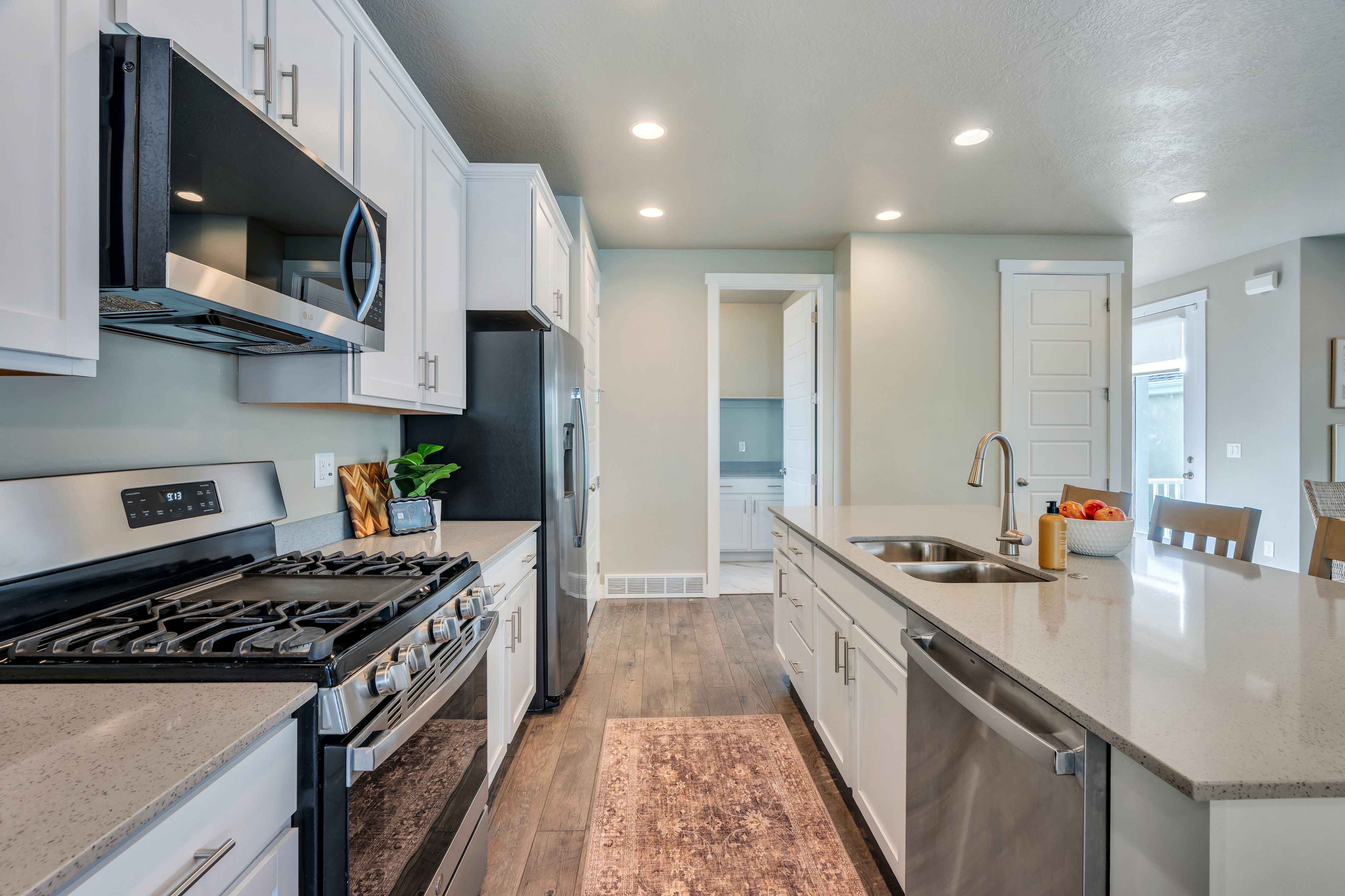 Modern kitchen featuring white shaker cabinetry, stainless steel appliances, light-toned countertops, wood-finish flooring, and recessed lighting