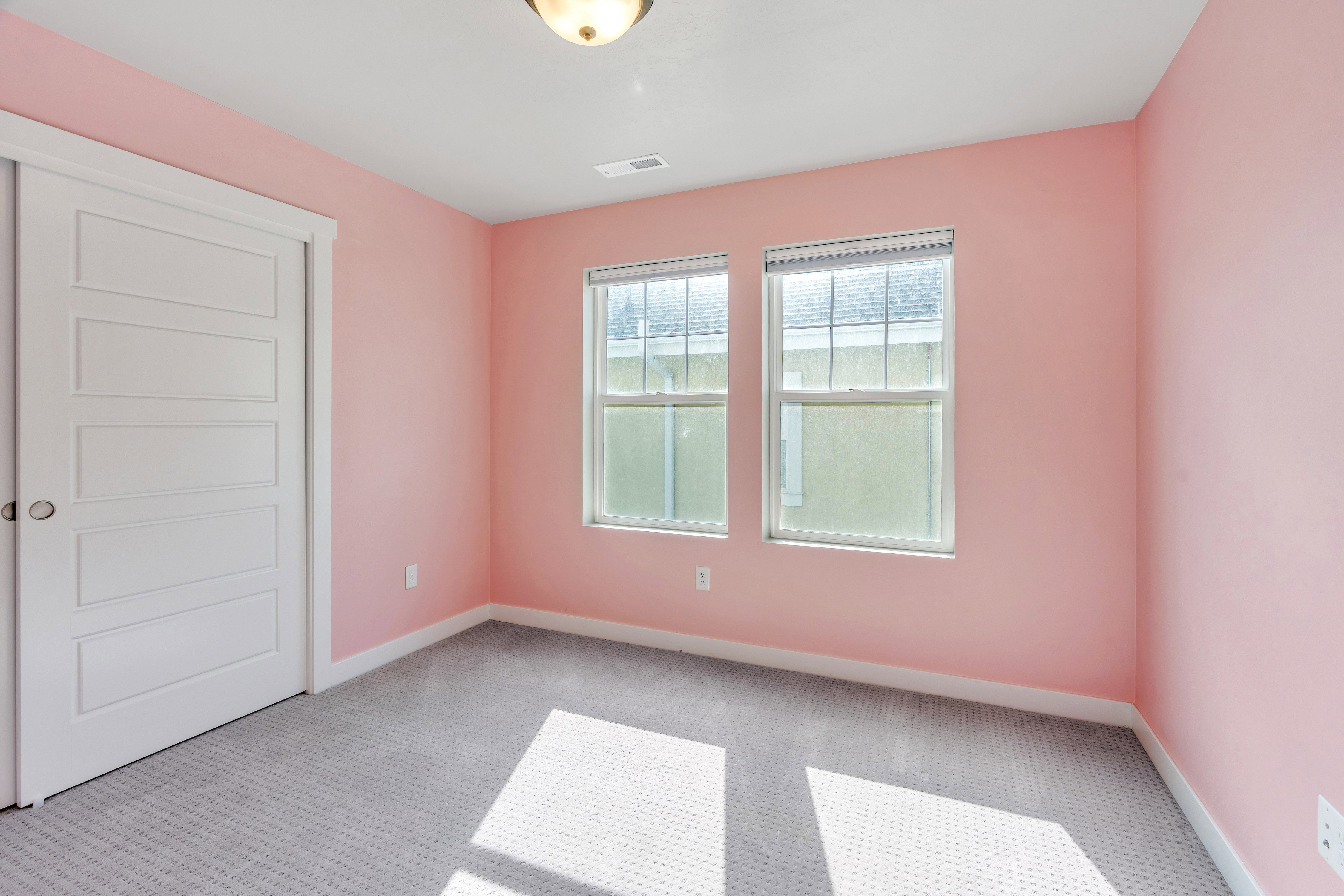 Room featuring two windows with blinds, a white paneled door, light pink walls, and gray patterned carpeting