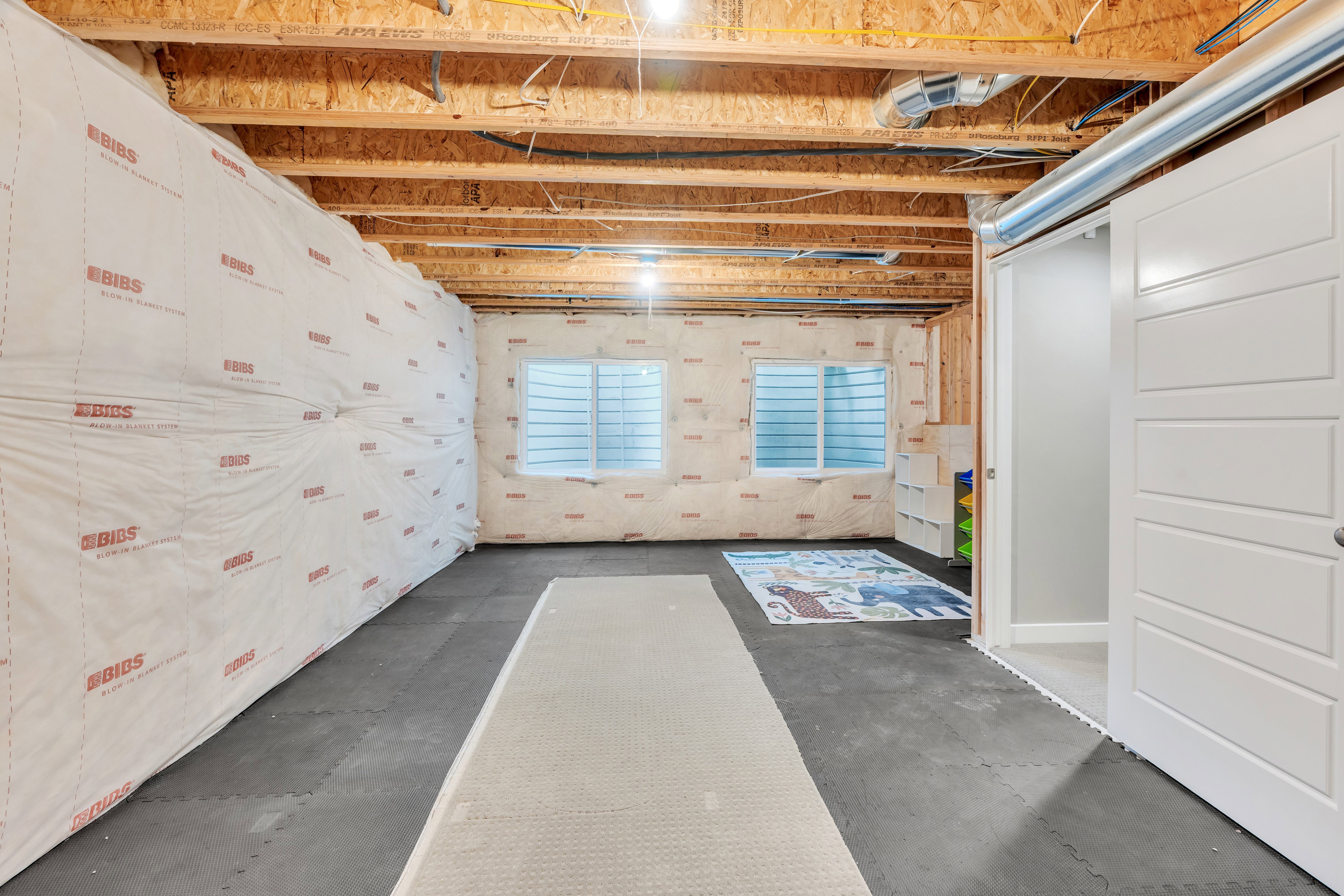 Unfinished basement with exposed wood joists and subfloor ceiling, two egress windows, and a sliding panel door