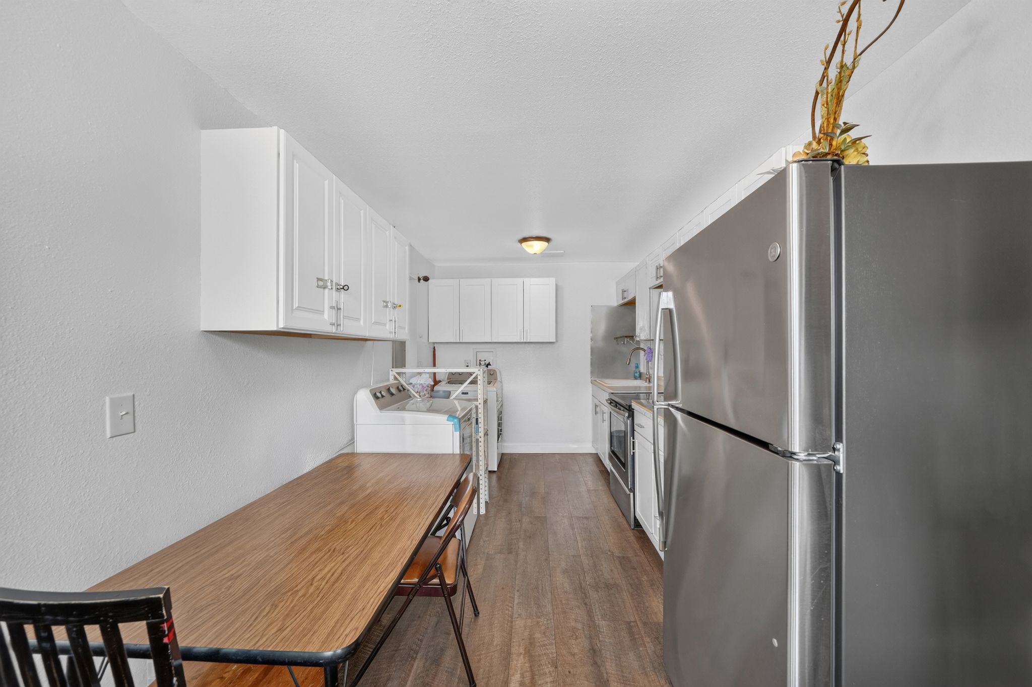 Galley-style kitchen featuring white cabinetry, stainless steel appliances, and wood-finish flooring