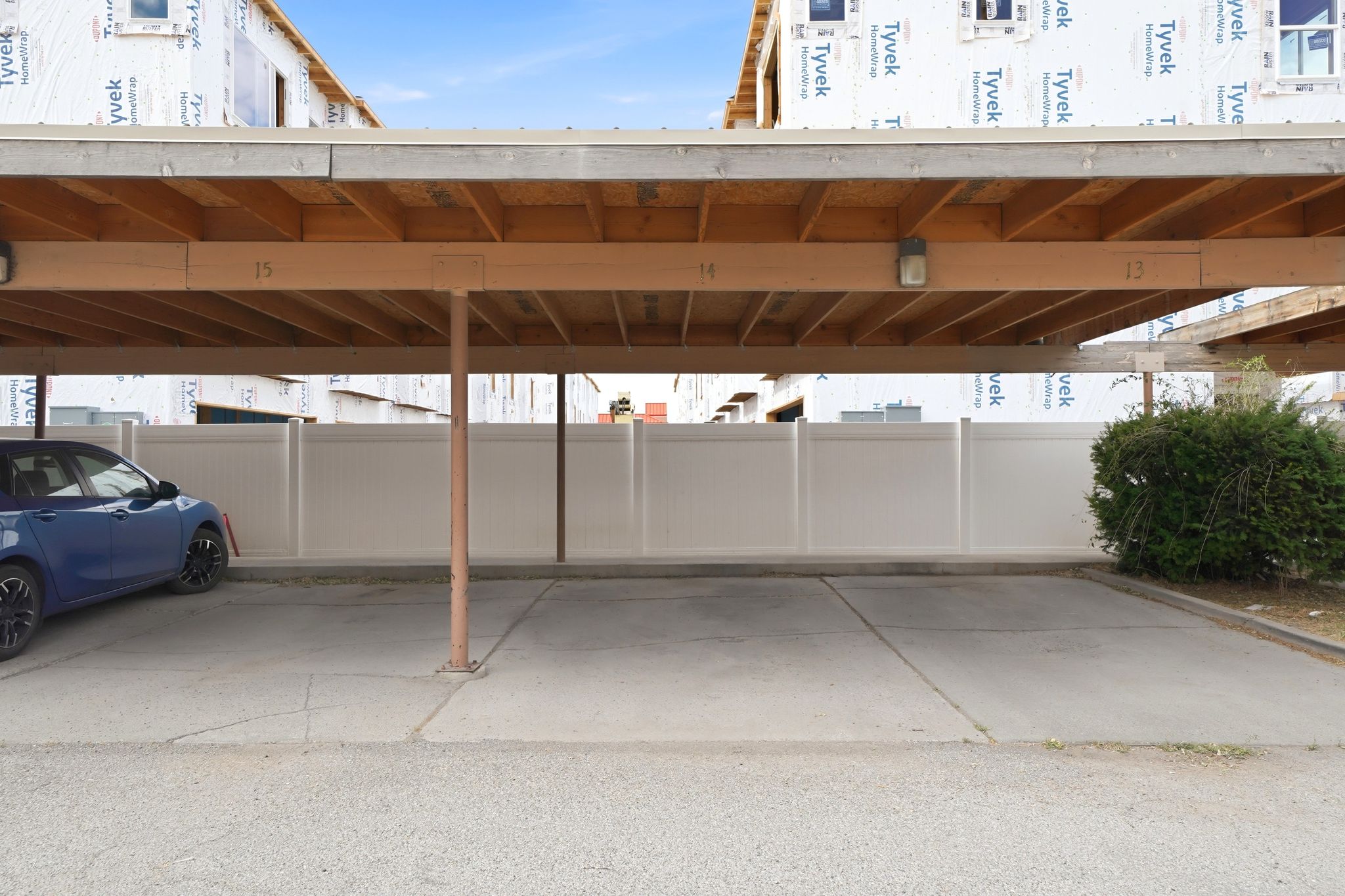 Covered parking space with concrete flooring, overhead wood beams, and built-in lighting fixtures