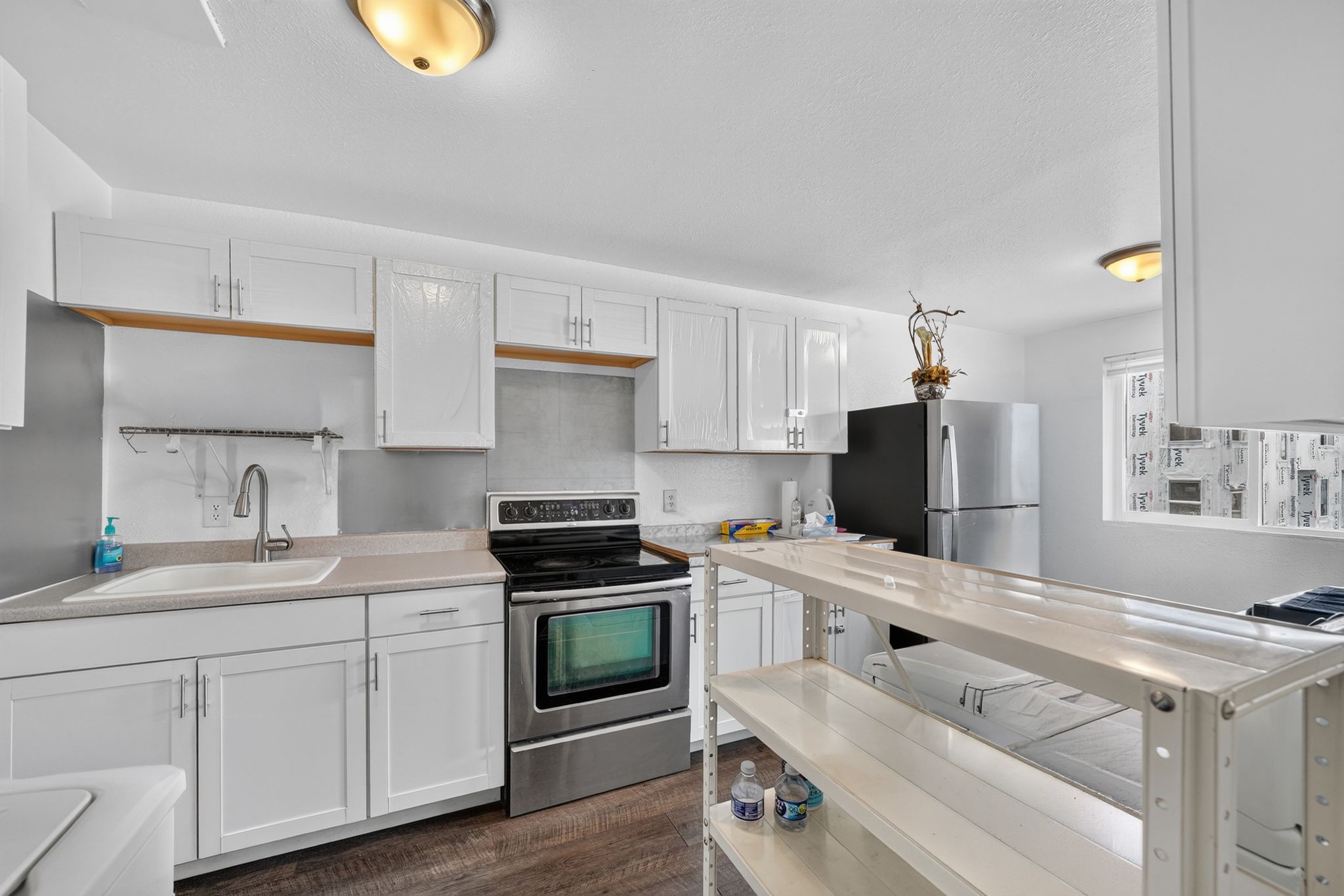 Kitchen featuring white shaker-style cabinetry, stainless steel appliances, light-toned countertops, and wood-finish flooring