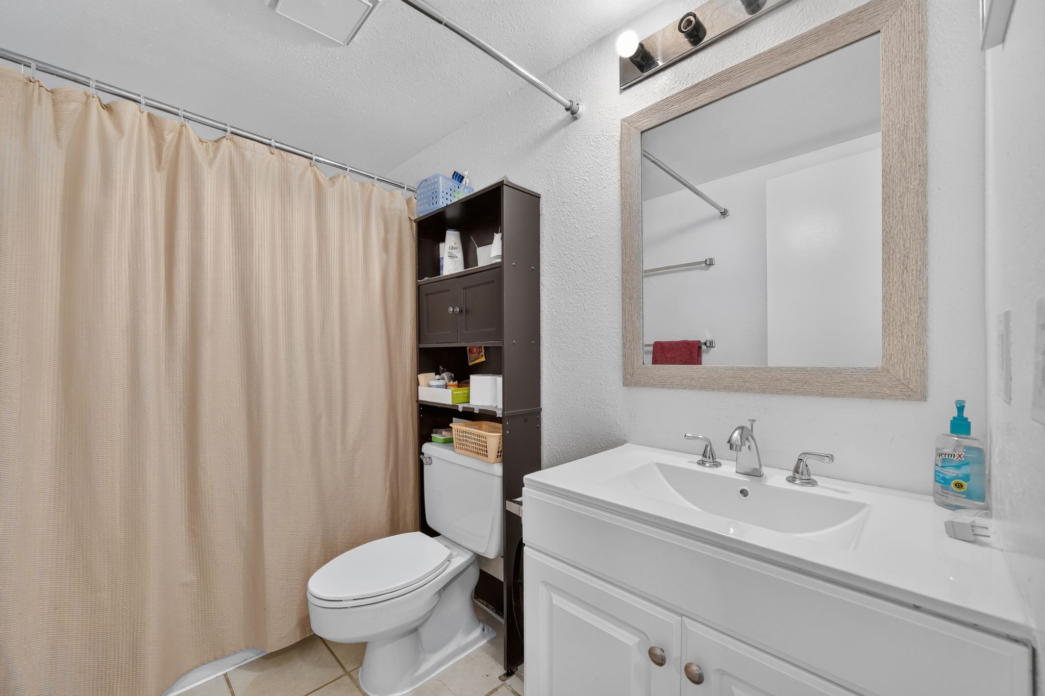 Bathroom vanity featuring a white countertop with an integrated sink, chrome faucet, and a framed mirror with overhead lighting