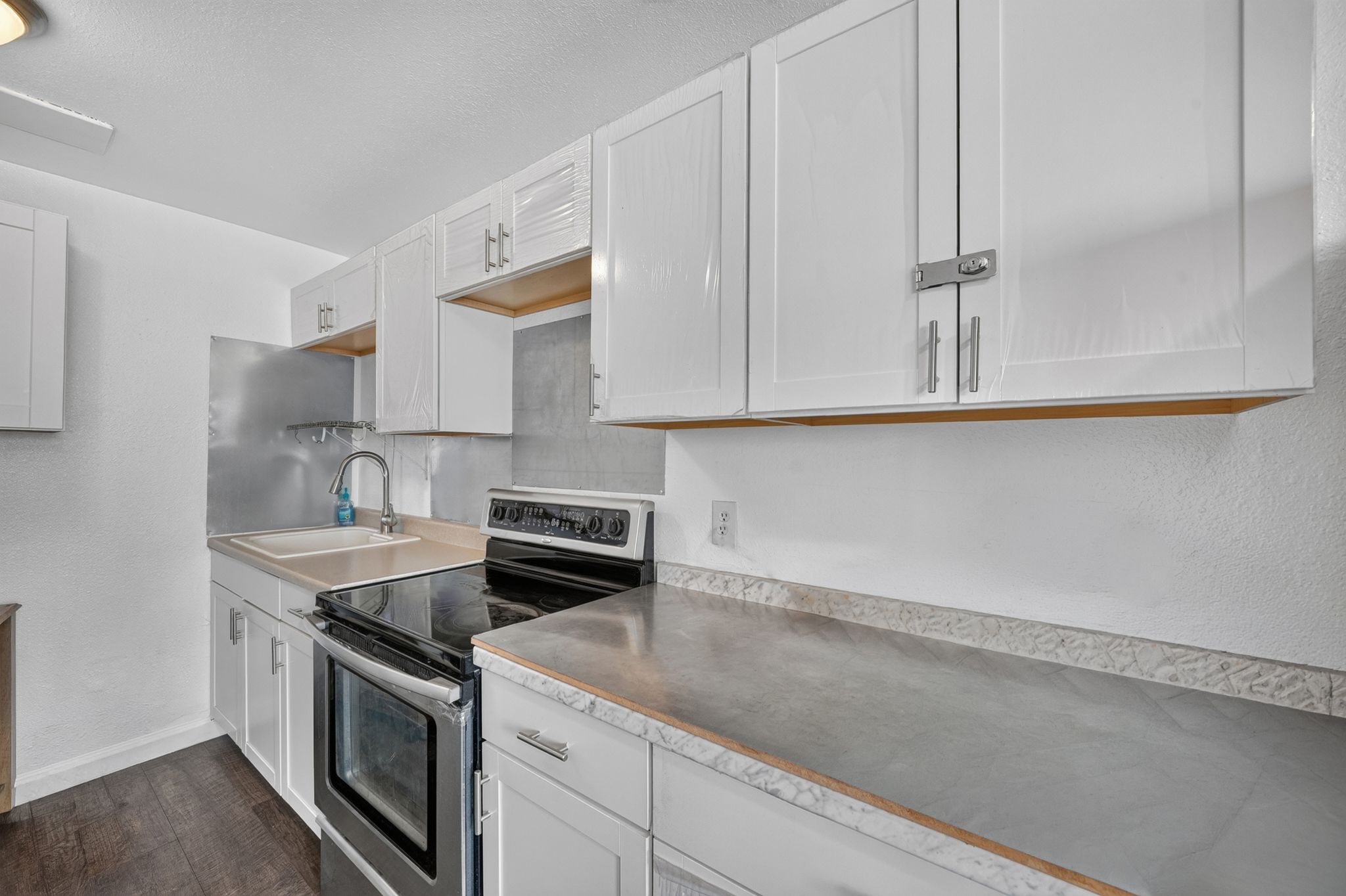 Kitchen featuring white cabinetry with brushed nickel pulls, dark wood-finish flooring, a stainless steel range, and light-toned countertops