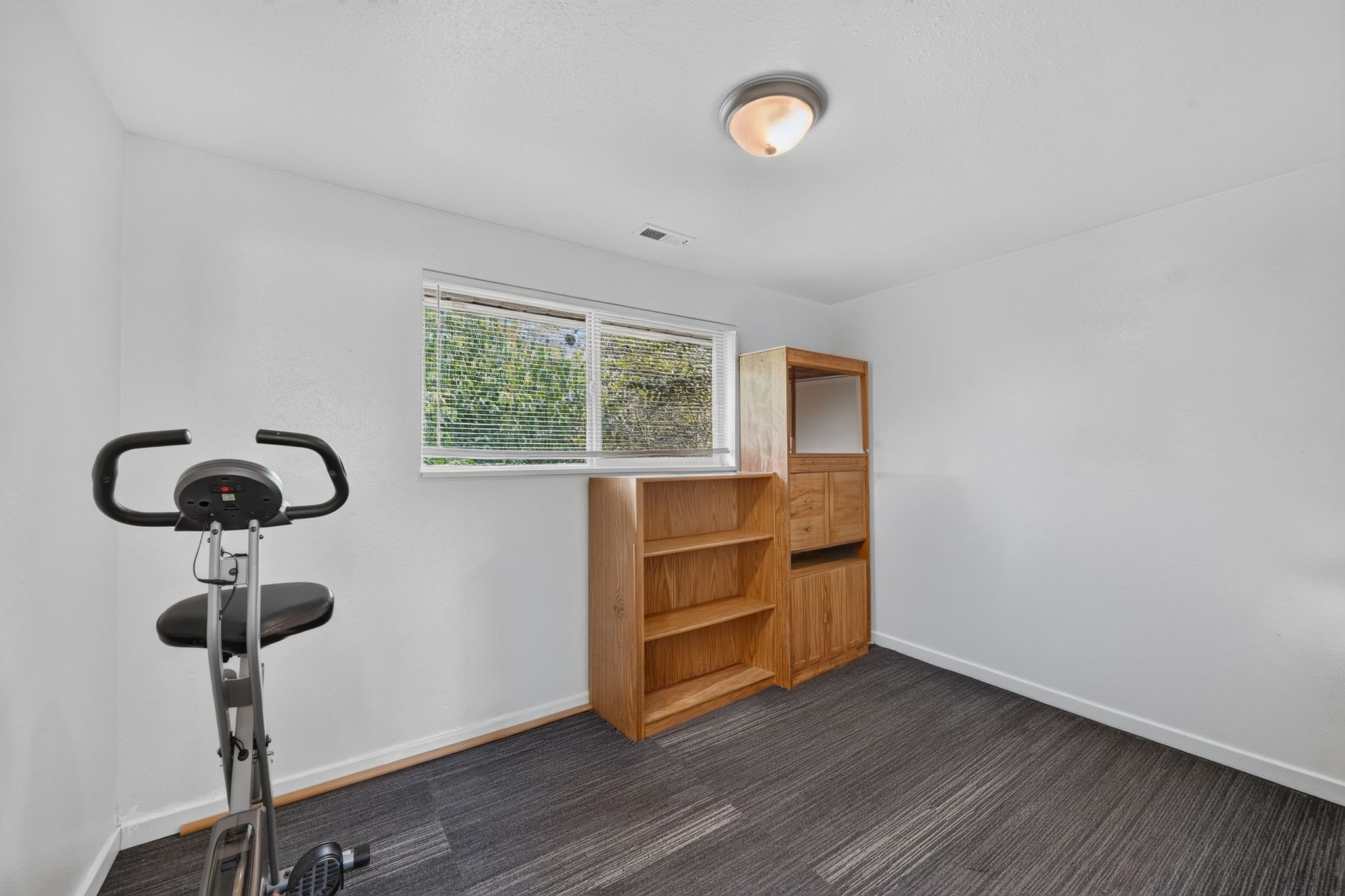 Room featuring a window with horizontal blinds, overhead lighting, and dark patterned carpeting