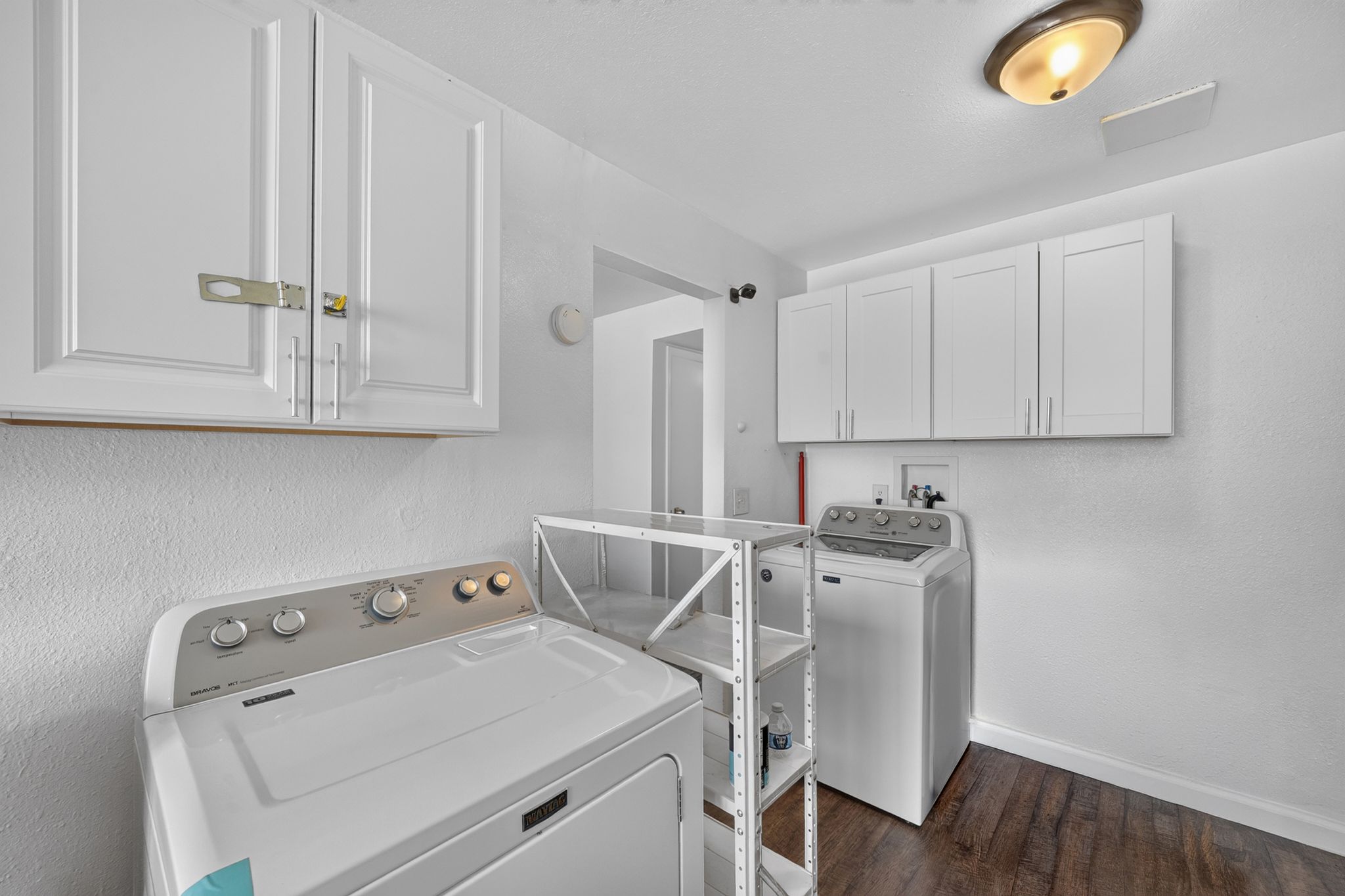 Dedicated utility space featuring overhead white cabinetry, wood-finish flooring, and a flush-mount ceiling light fixture