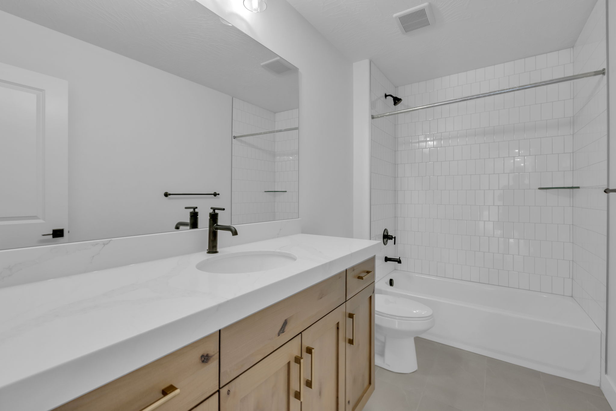 Bathroom #3, featuring a light wood-finish vanity with gold-tone hardware, a white Quartz countertop, and a large wall-mounted mirror.