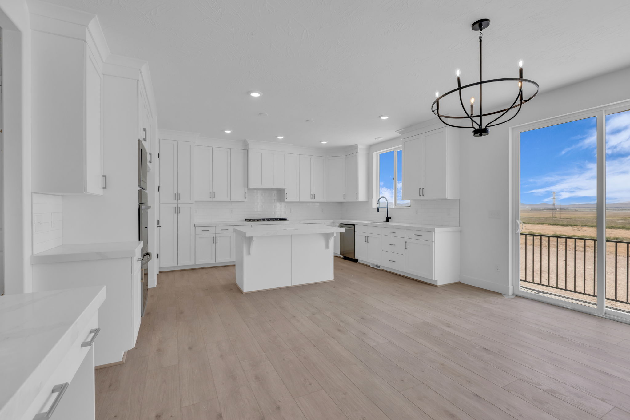 Bright kitchen featuring full-height white cabinetry, a central island, LED lighting, large sliding glass door to back deck and contemporary chandelier over the dining area.