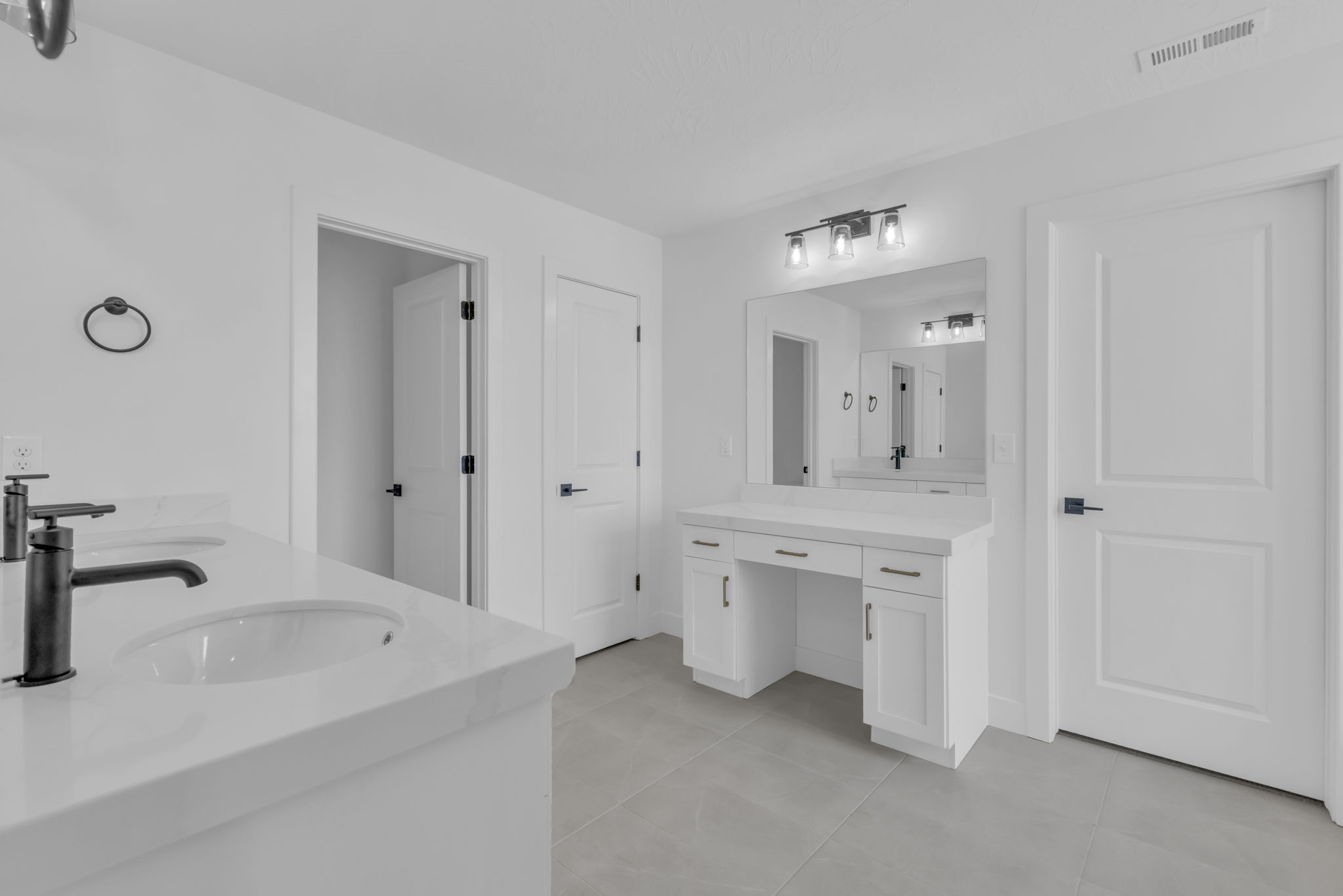 Spacious primary bathroom #1 featuring dual vanities with white Quartz countertops and matte black faucets, a dedicated makeup vanity with built-in storage, and a large wall-mounted mirror with integrated lighting.