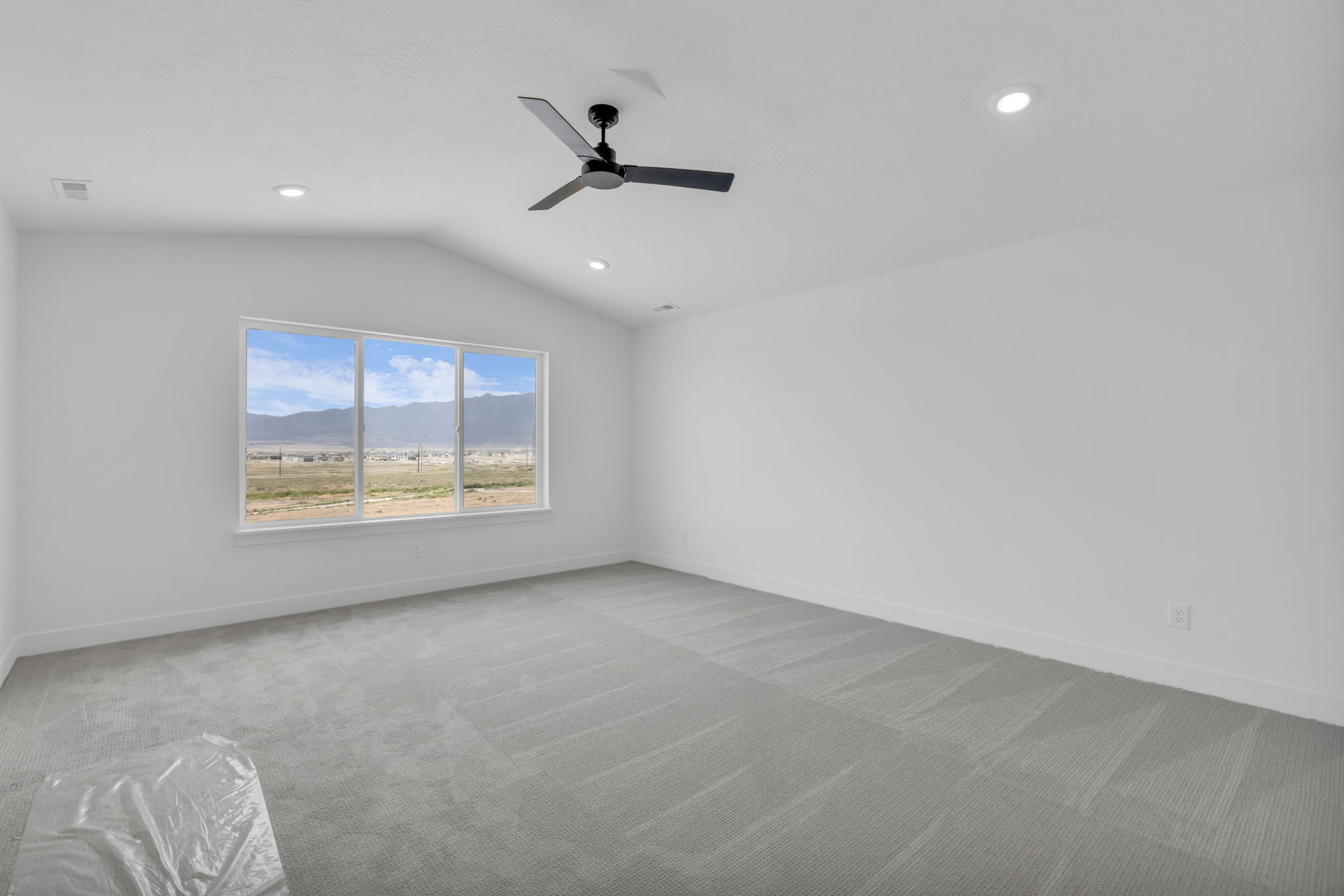 Vaulted primary  bedroom featuring a three-panel large window with a mountain backdrop, LED lighting, contemporary ceiling fan.