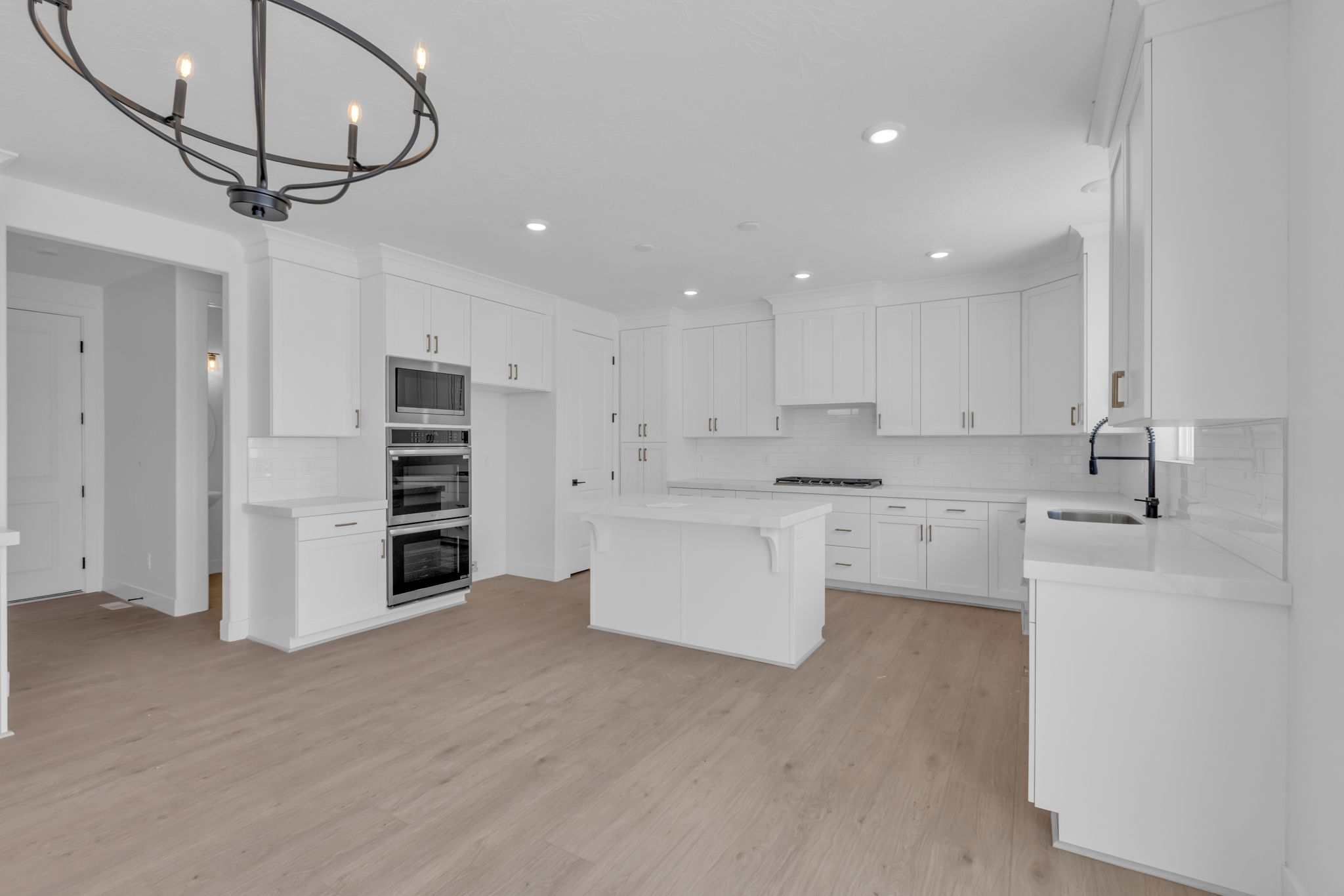 Bright kitchen featuring full-height white cabinetry, a central island, LED lighting, professional grade appliances including double oven, microwave, dishwasher and gas cooktop.